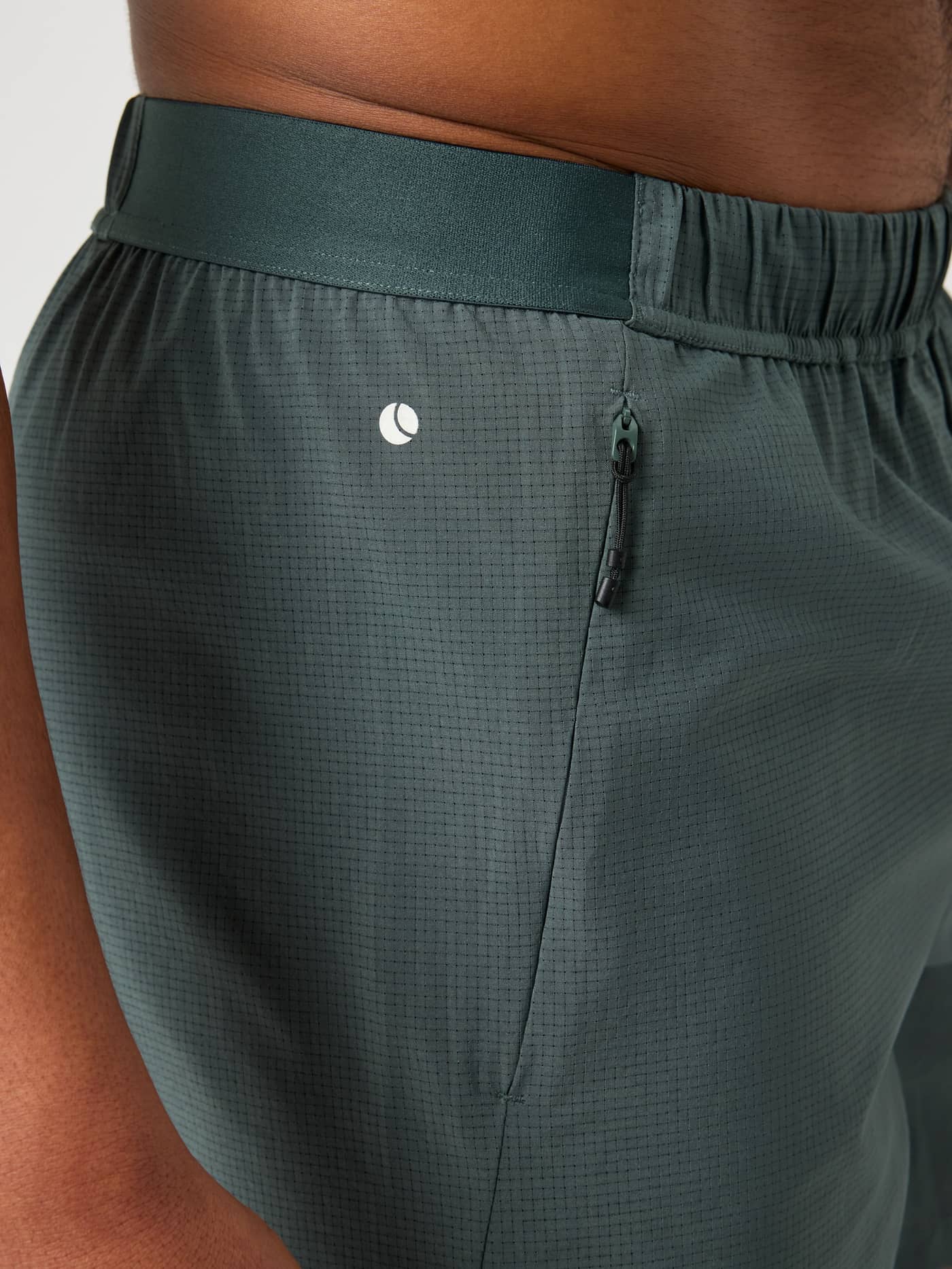 Close-up of the Urban Chic (Green) Borg Zip Shorts 7 Inch, featuring a white tennis logo and zip pocket for training. - Image 4