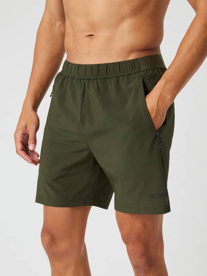 Front view of a model wearing the Borg Zip 7" Shorts in Forest Night green, with one hand in the side pocket.