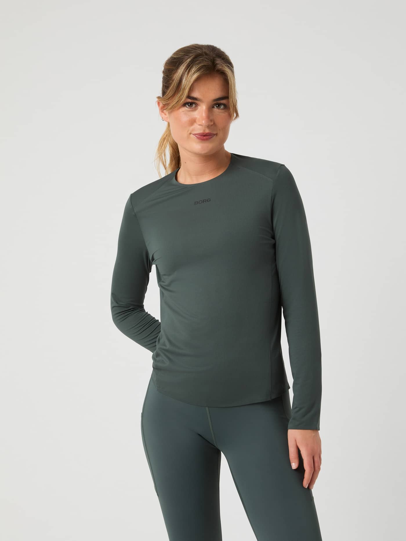 Front view of a woman in the regular-fit Urban Chic (Green) Borg Running Feather Long Sleeve T-Shirt with a black logo. - Image 1