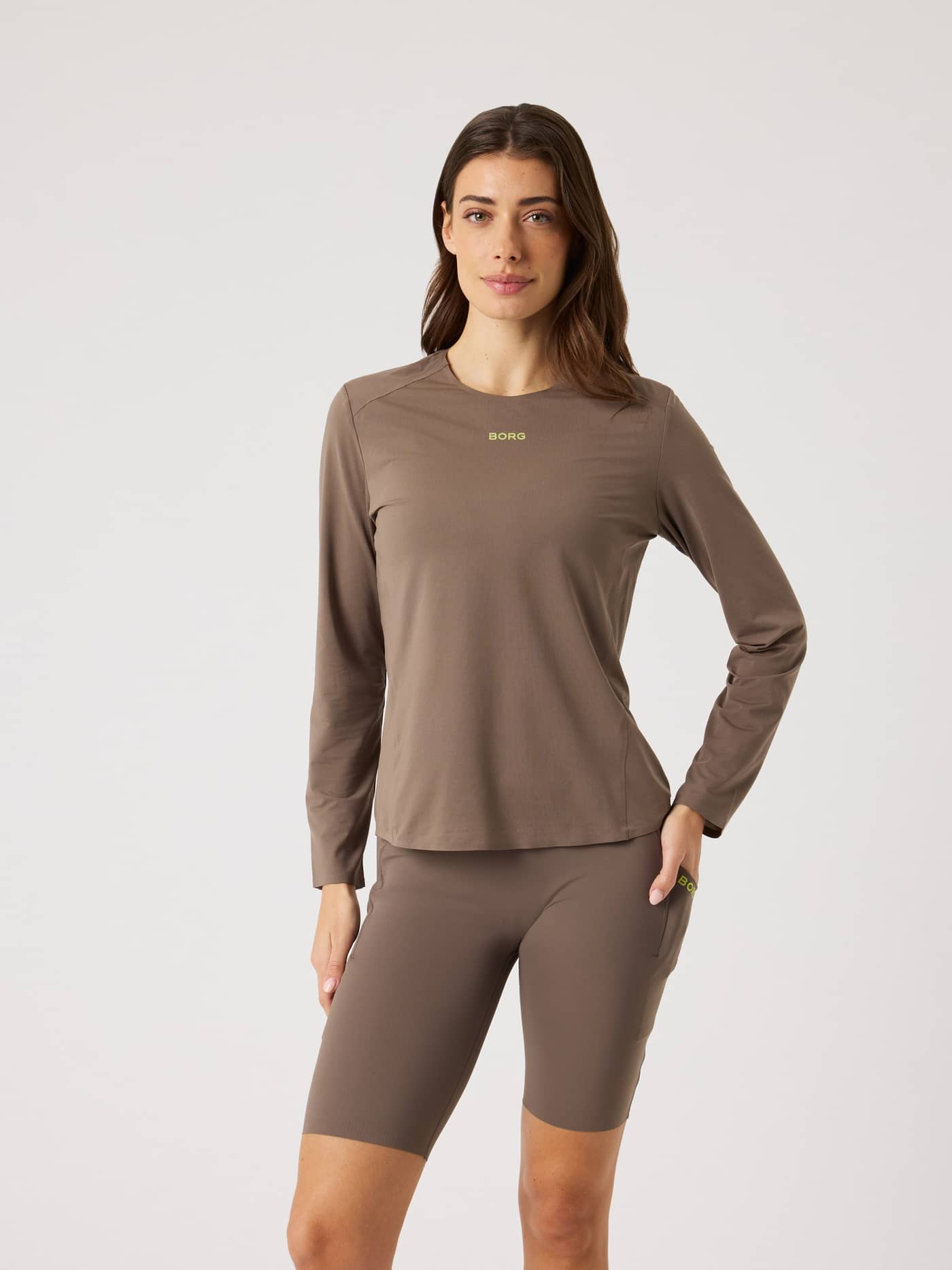 Vista frontal de una mujer con la Borg Running Feather Long Sleeve T-Shirt en Falcon (Marrón) con logo verde lima de running. - Image 2