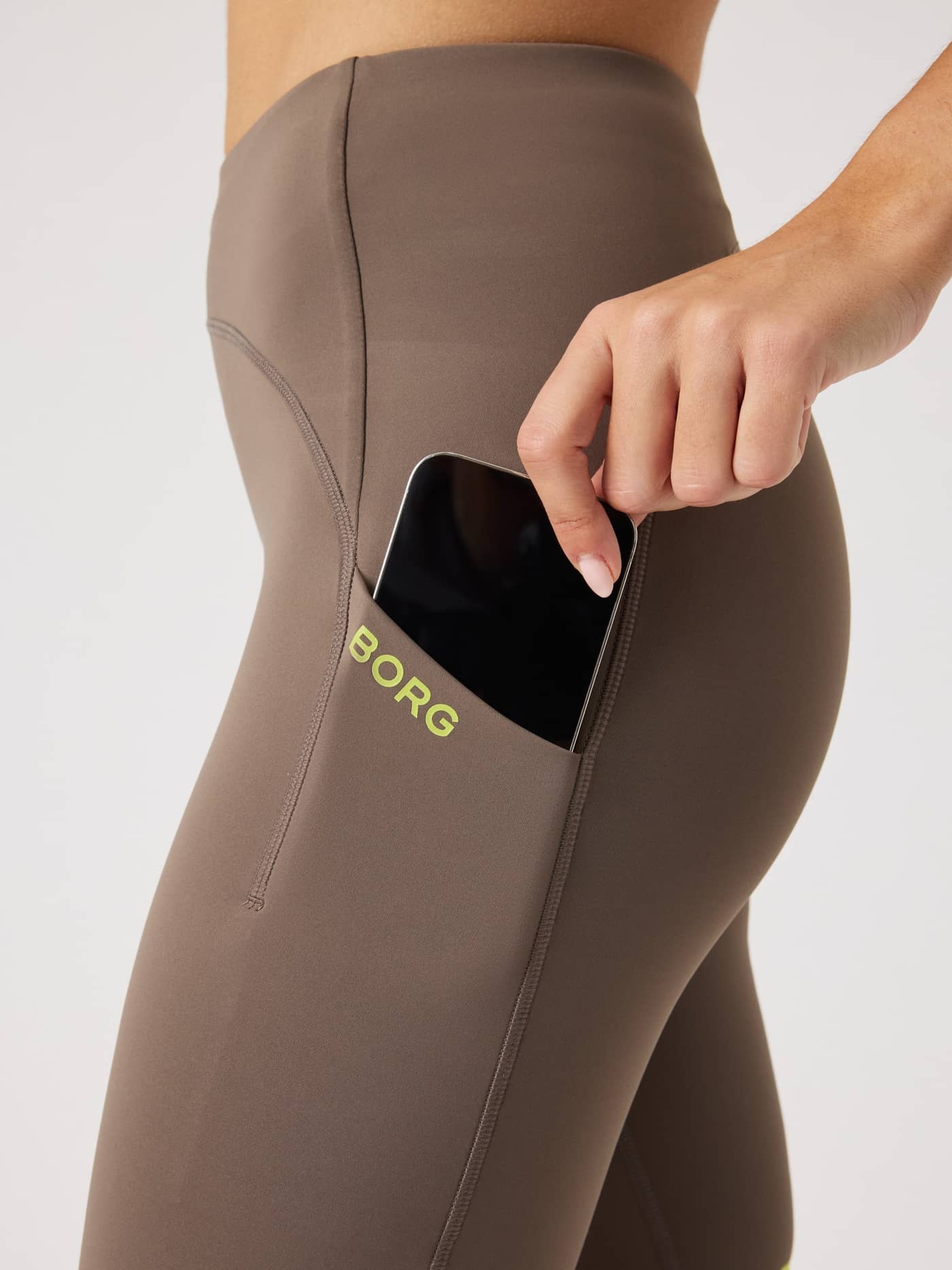 Side phone pocket on the Falcon (Brown) Borg Performance Short Tights for women, featuring a lime logo and sleek running fit. - Image 5