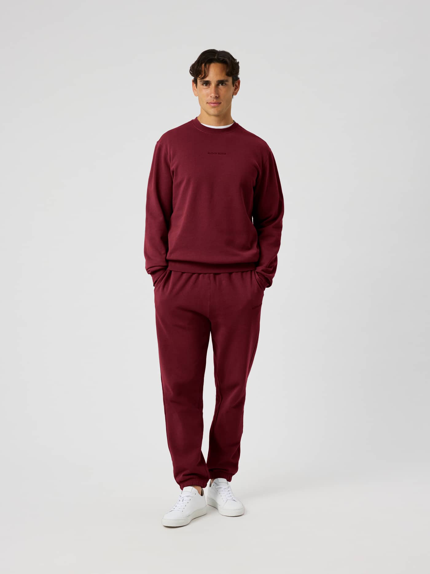 Front view of the Borg Classic Sweatpants in Cabernet (red) on a male model wearing matching sweatshirt and white sneakers. - Image 3