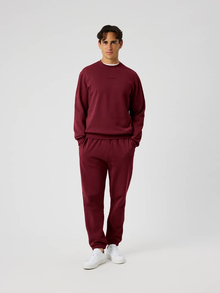 Front view of the Borg Classic Sweatpants in Cabernet (red) on a male model wearing matching sweatshirt and white sneakers.