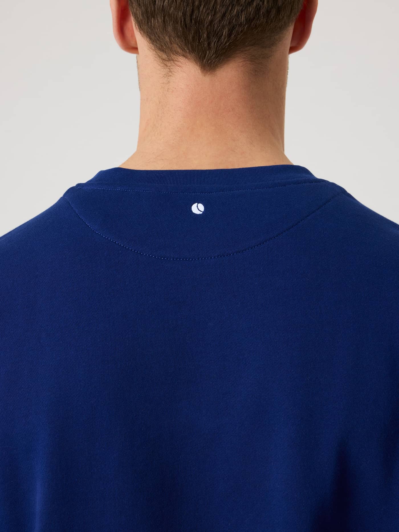 Detalle de la nuca de la Borg Classic Sweatshirt en Blue Depths (Azul) con el logo de pelota de tenis blanco. - Image 4