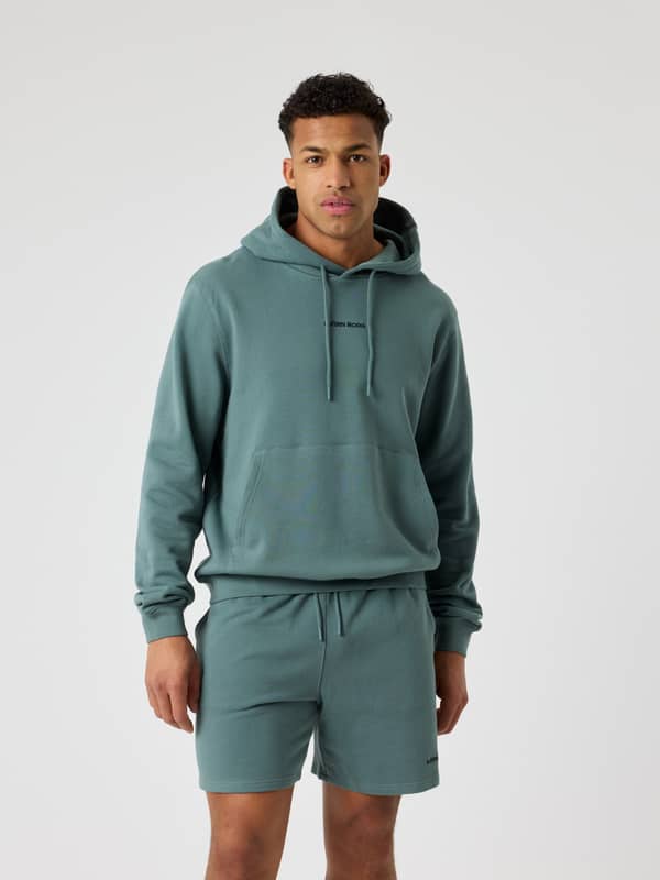 Vue de face d'un homme portant le Borg Classic Hoodie en coton Balsam Green (Vert) avec logo noir et poche kangourou.