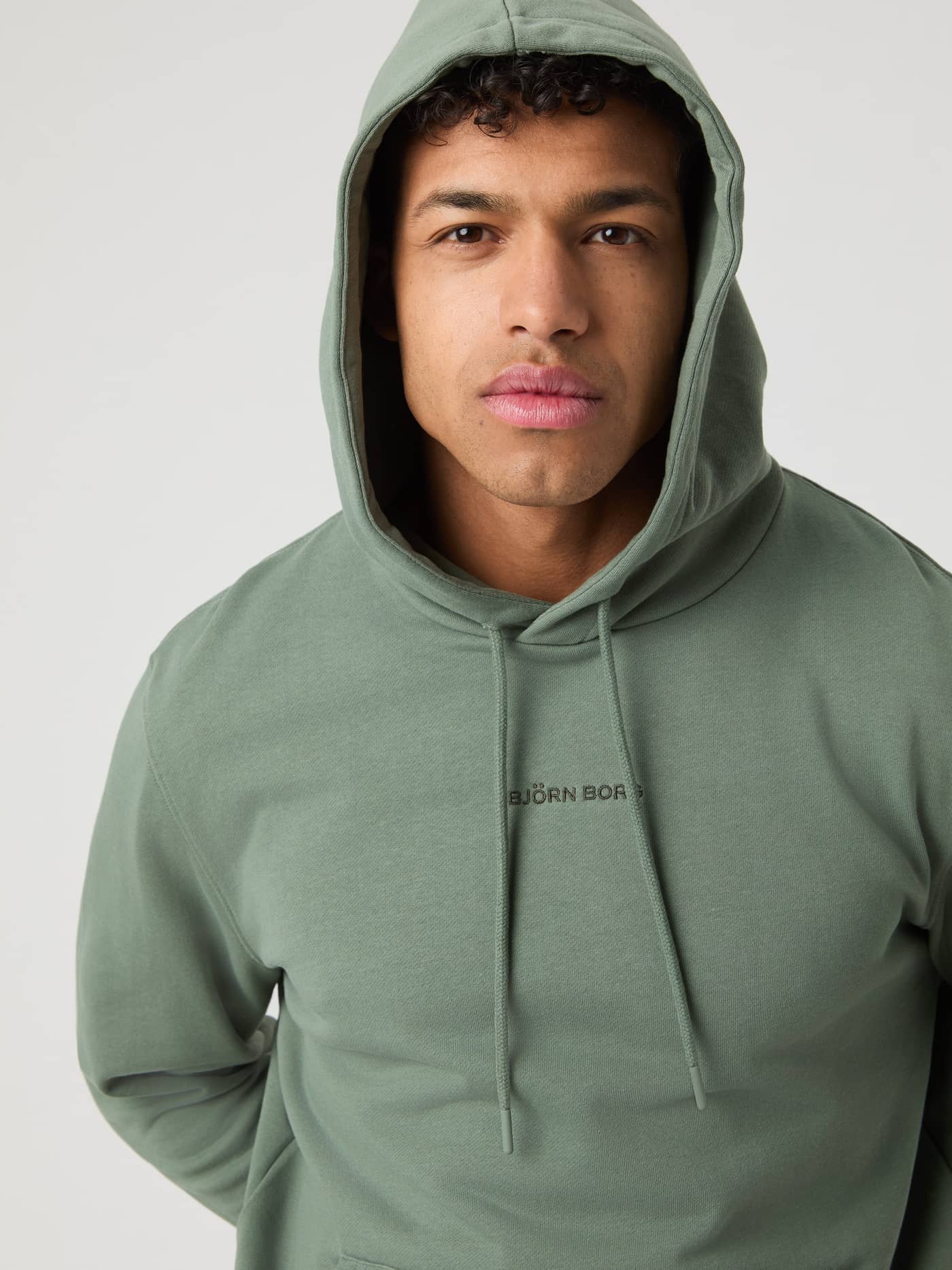 Nahaufnahme eines Mannes im Borg Classic Hoodie in Agave Green (Grün) mit tonalem, besticktem Logo für Stil und Funktion. - Image 4