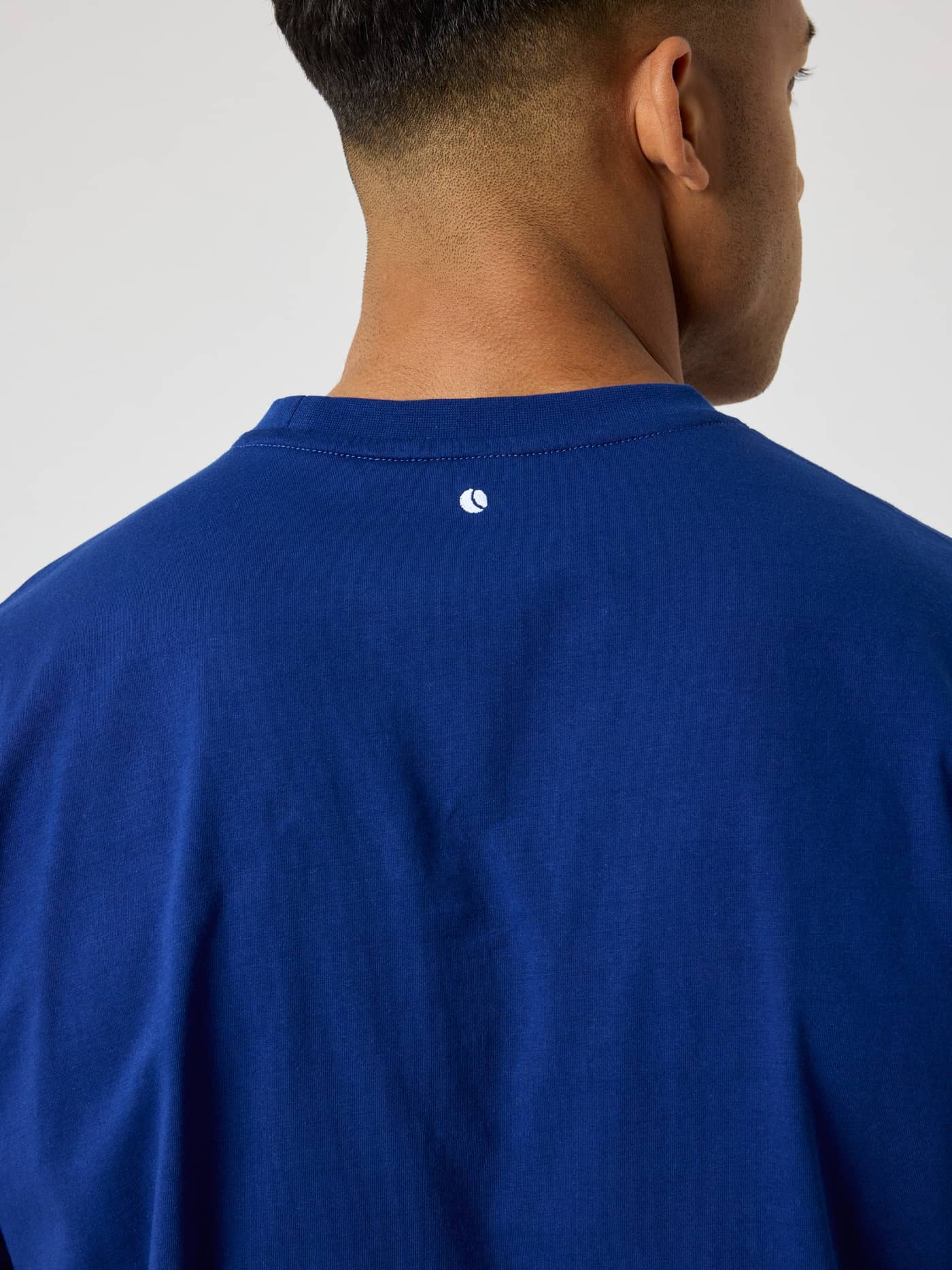 Nahaufnahme der Rückansicht des Borg Classic T-Shirt in Blue Depths (Blau) mit weiß gesticktem Tennisball-Logo. - Image 4
