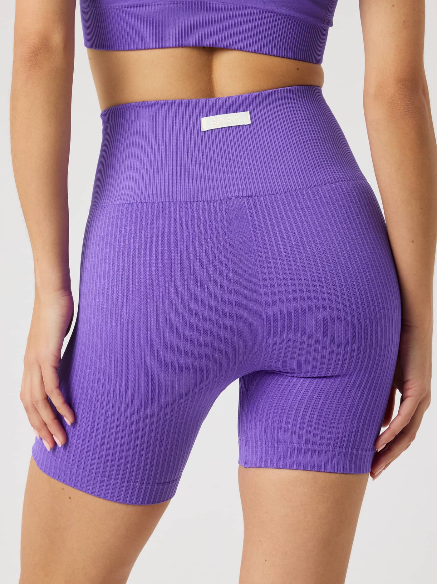 Achteraanzicht van de Studio Seamless Ribbed Shorts in Simply Purple (Paars) voor training met een wit logolabel. - Image 2