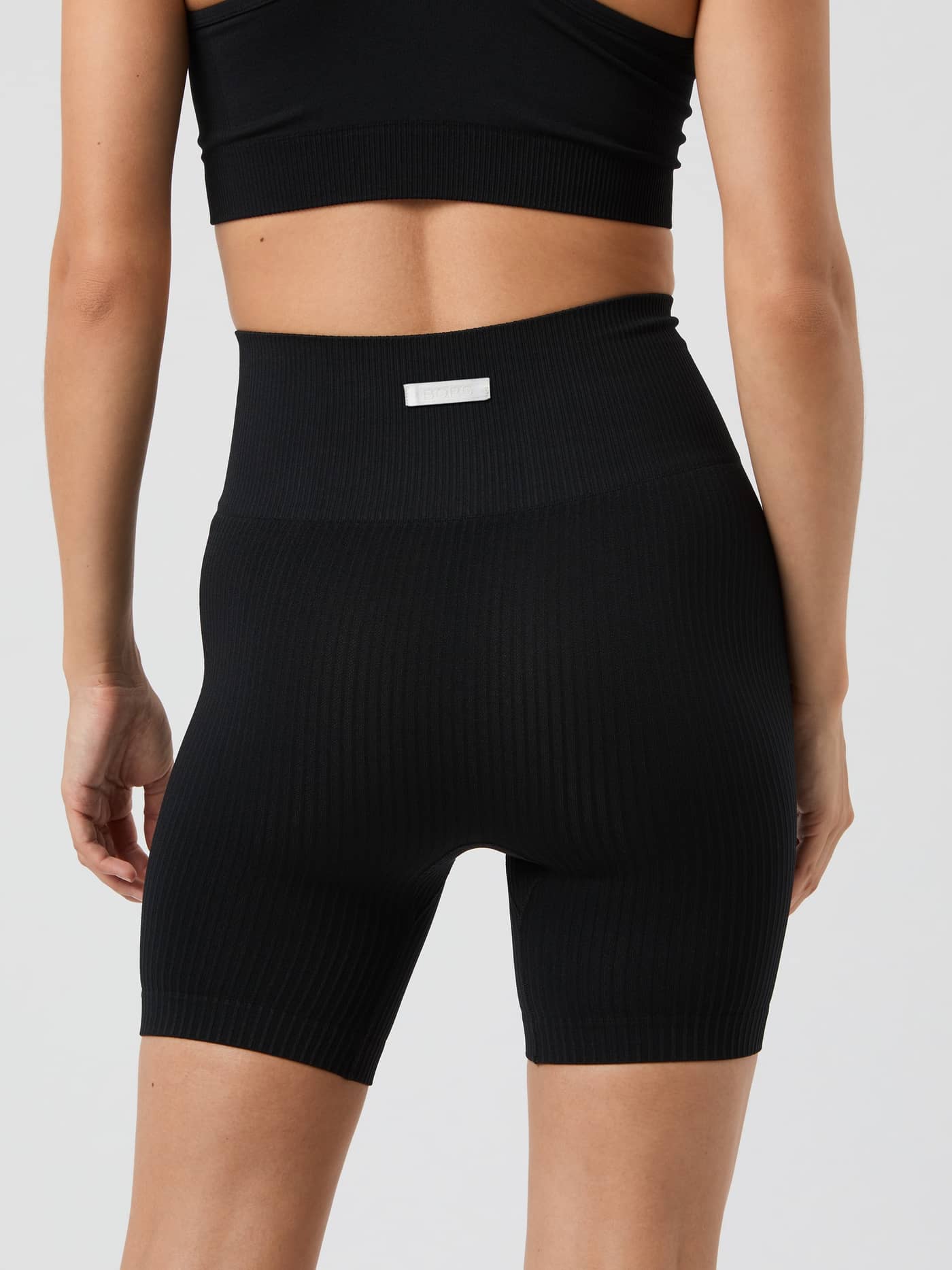 Back view of a model wearing the Studio Seamless Ribbed Shorts in Black Beauty (Black) for training with a white logo label. - Image 3
