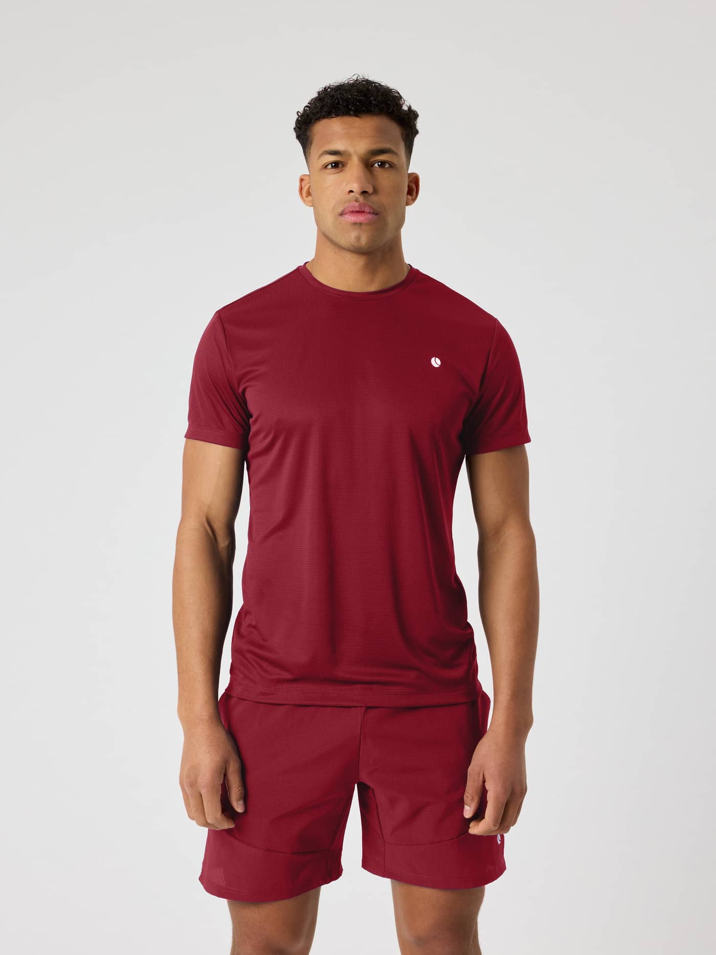 Männliches Model trägt das Ace Light T-Shirt in Cabernet (Rot) mit einem weißen Logo für Tennis. - Image 1