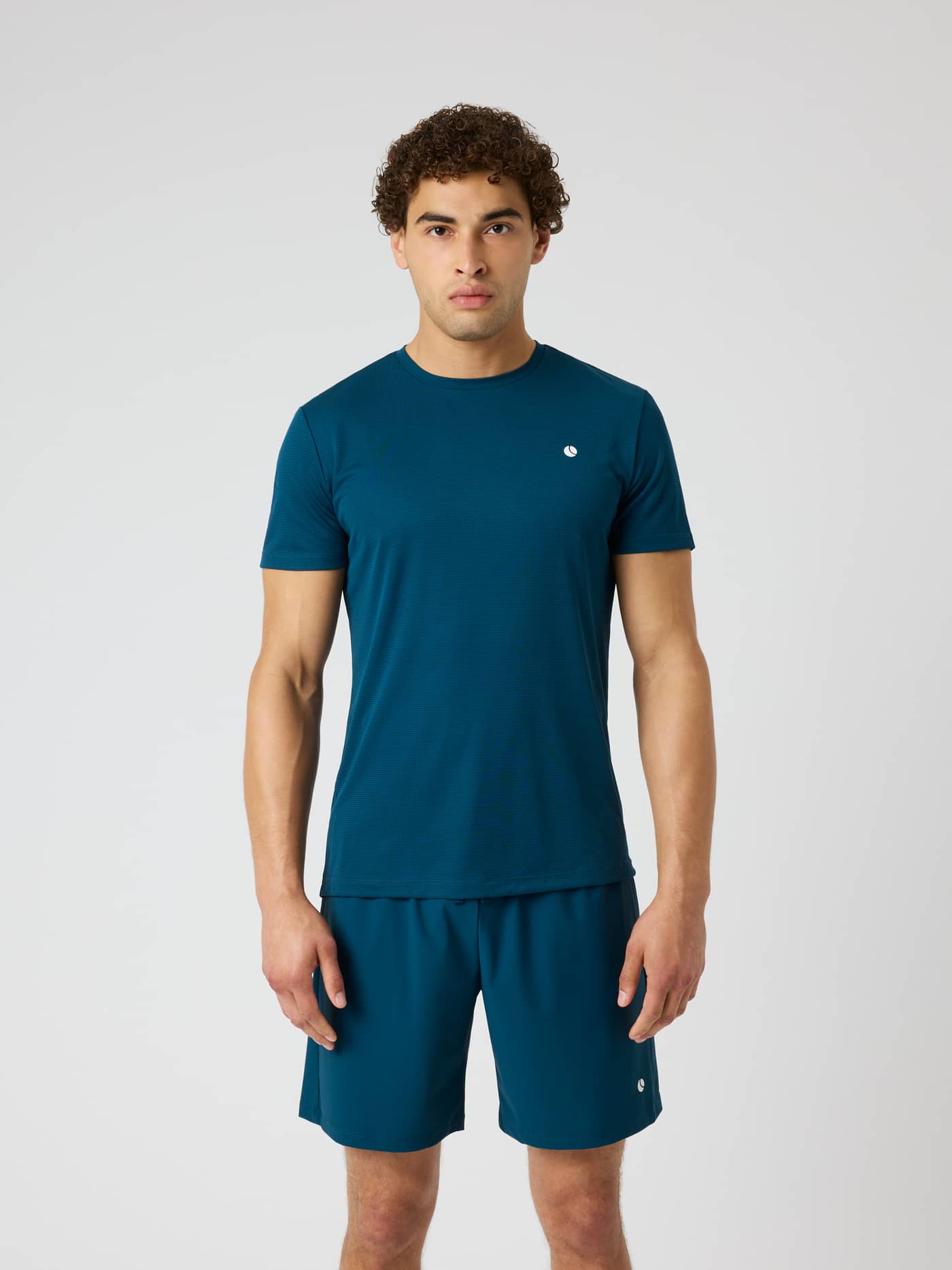 Front view of a man wearing the Ace Light T-Shirt in Reflecting Pond (Green) featuring a white tennis logo. - Image 1