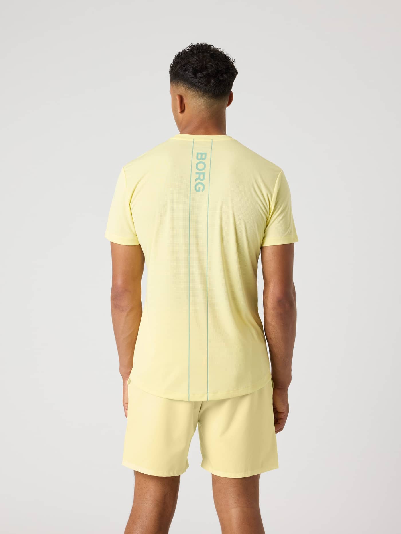 Back view of a man wearing the Ace Light T-Shirt in Lemonade (Yellow) with a BORG logo stripe for tennis performance. - Image 2