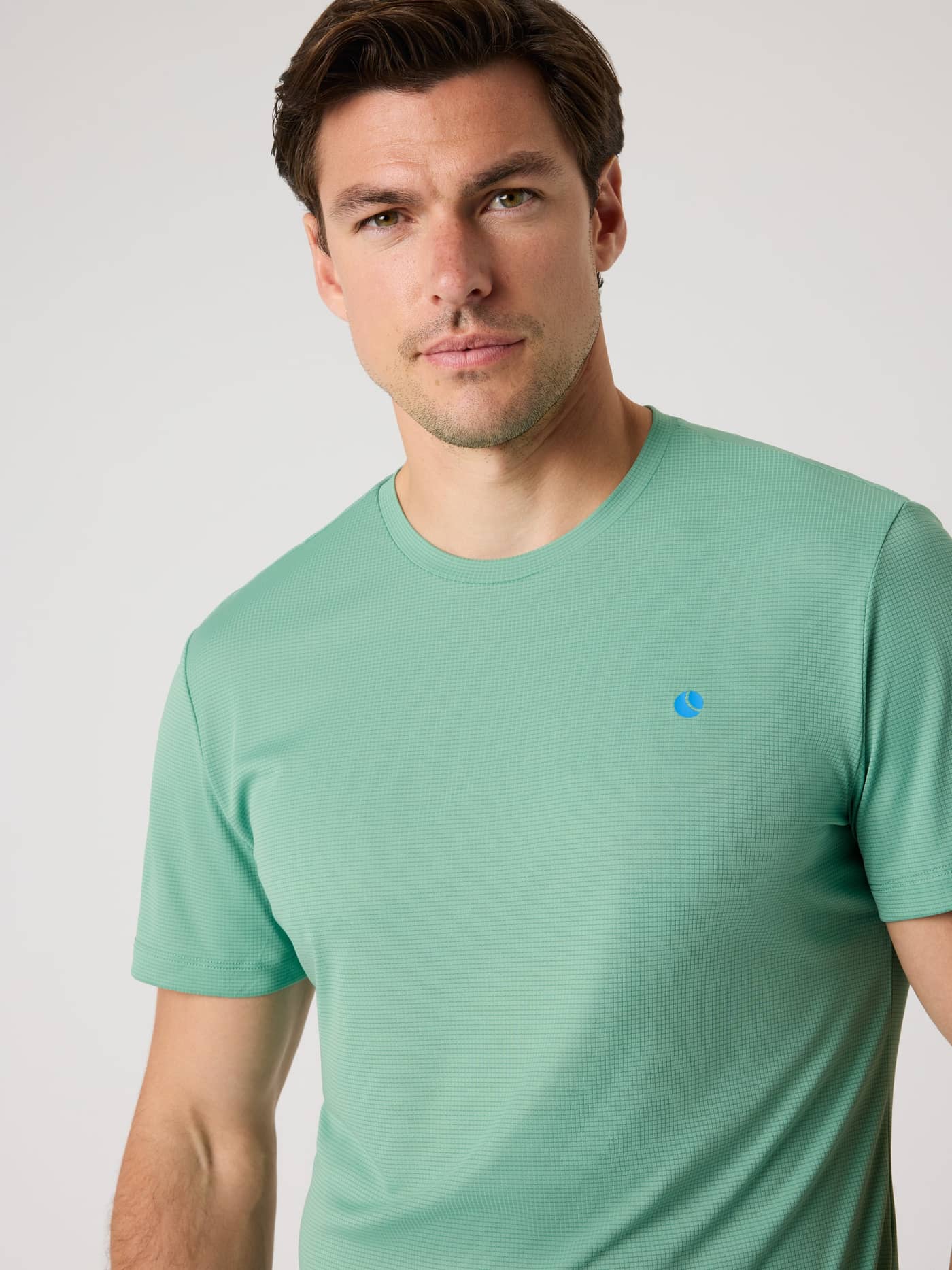 Front close-up of a man wearing the Björn Borg Ace Light T-Shirt in Malachite Green (Green) with a blue tennis ball logo. - Image 5
