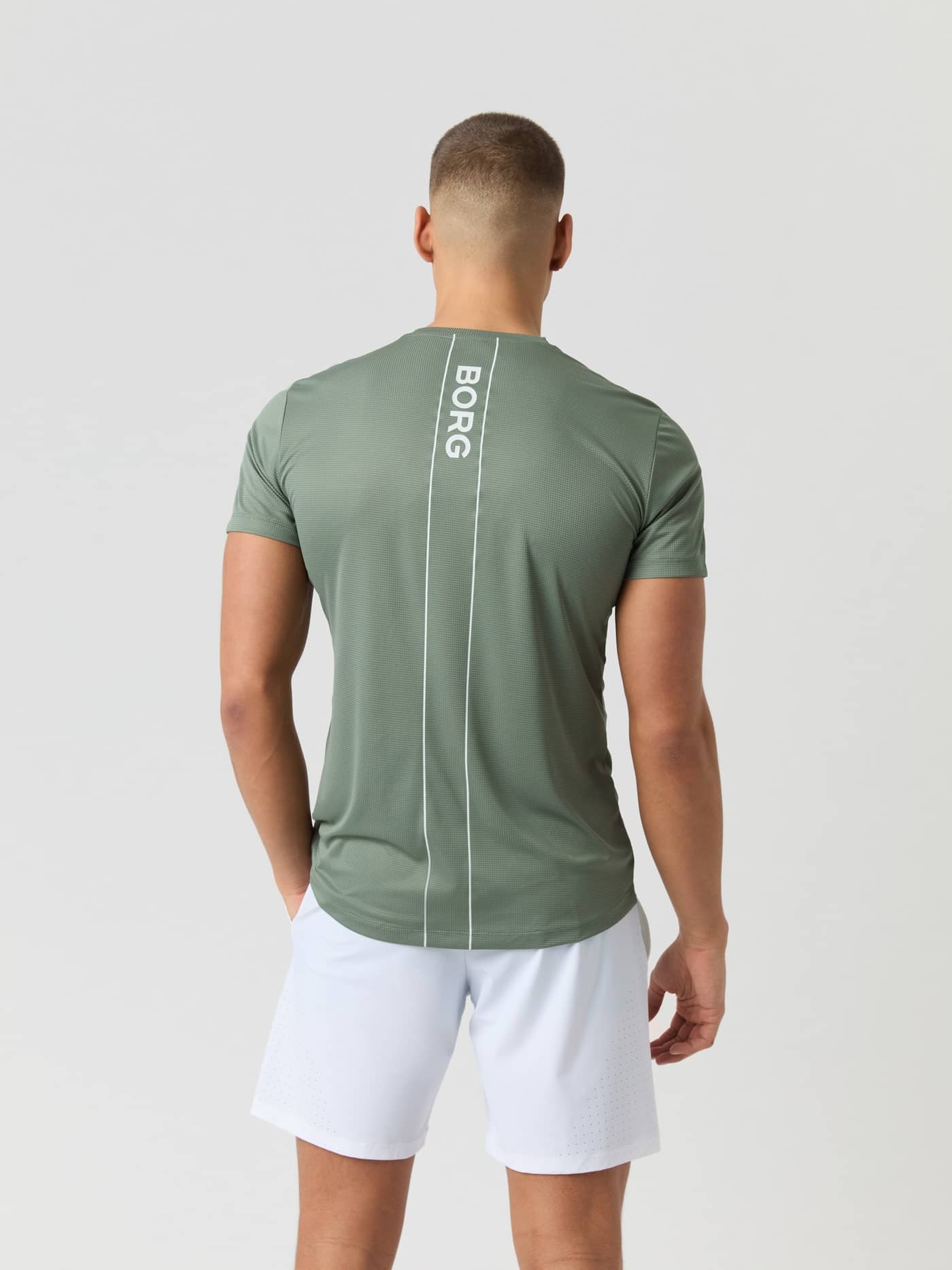 Back view of a model wearing the Björn Borg Ace Light T-shirt in Agave Green, paired with white shorts. - Image 2