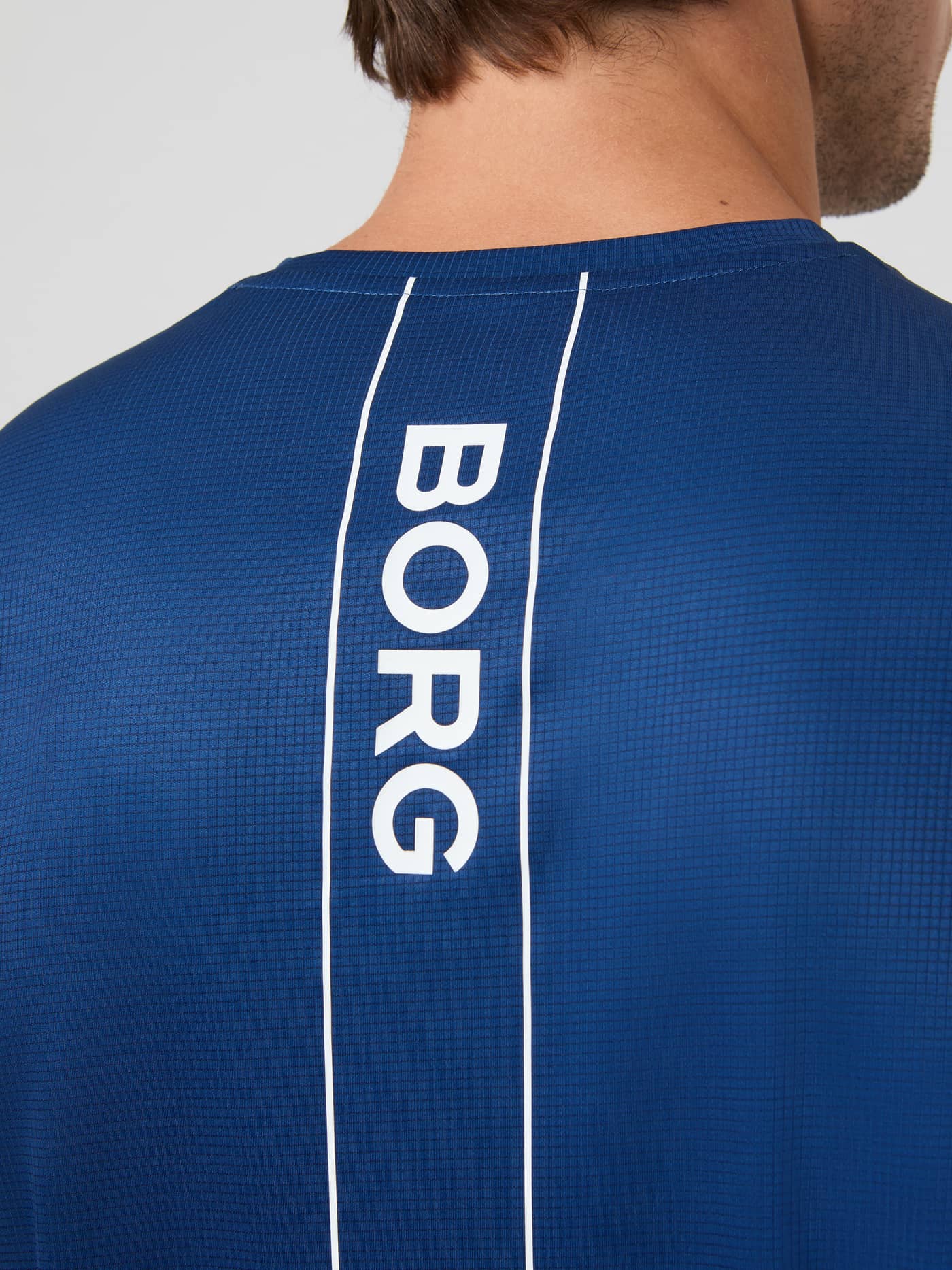 Close-up of the vertical BORG logo and textured fabric on the back of the men's blue Ace Light T-Shirt. - Image 4
