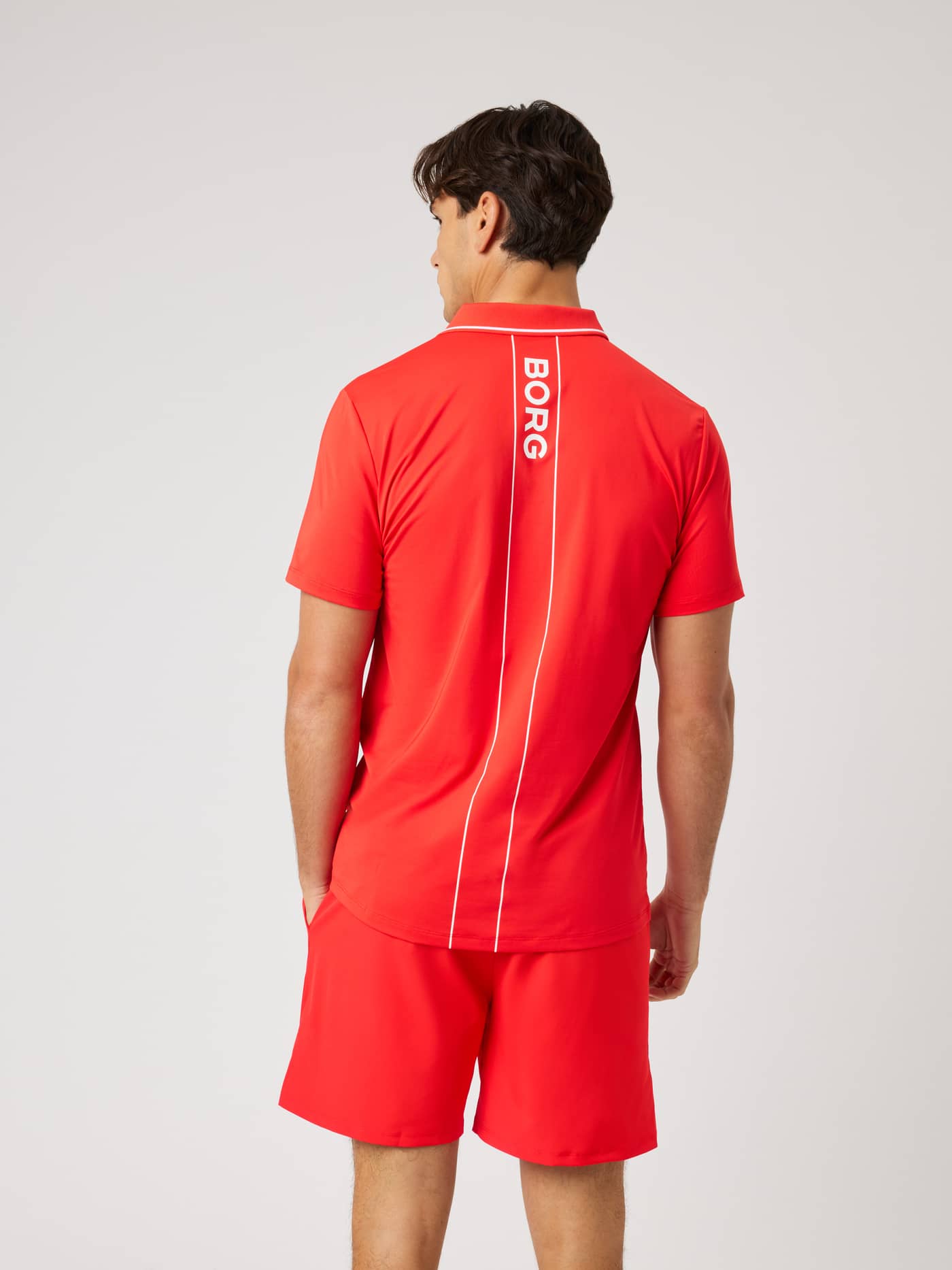Back view of a model wearing the Ace Polo Shirt in Flame Scarlet (Red) with a white Borg logo for tennis. - Image 3