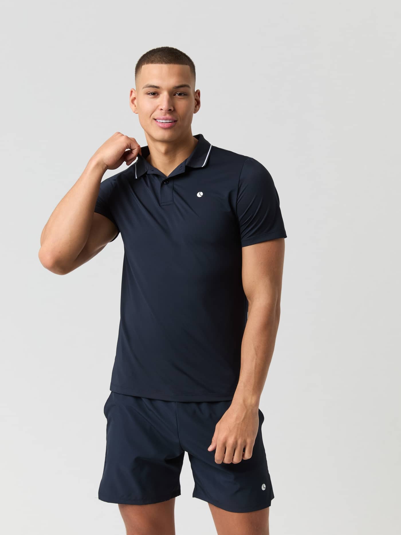 Ace Polo Shirt i Night sky (Marineblå) set forfra med hvidt logo og matchende shorts, ideel til tennis og performance. - Image 1