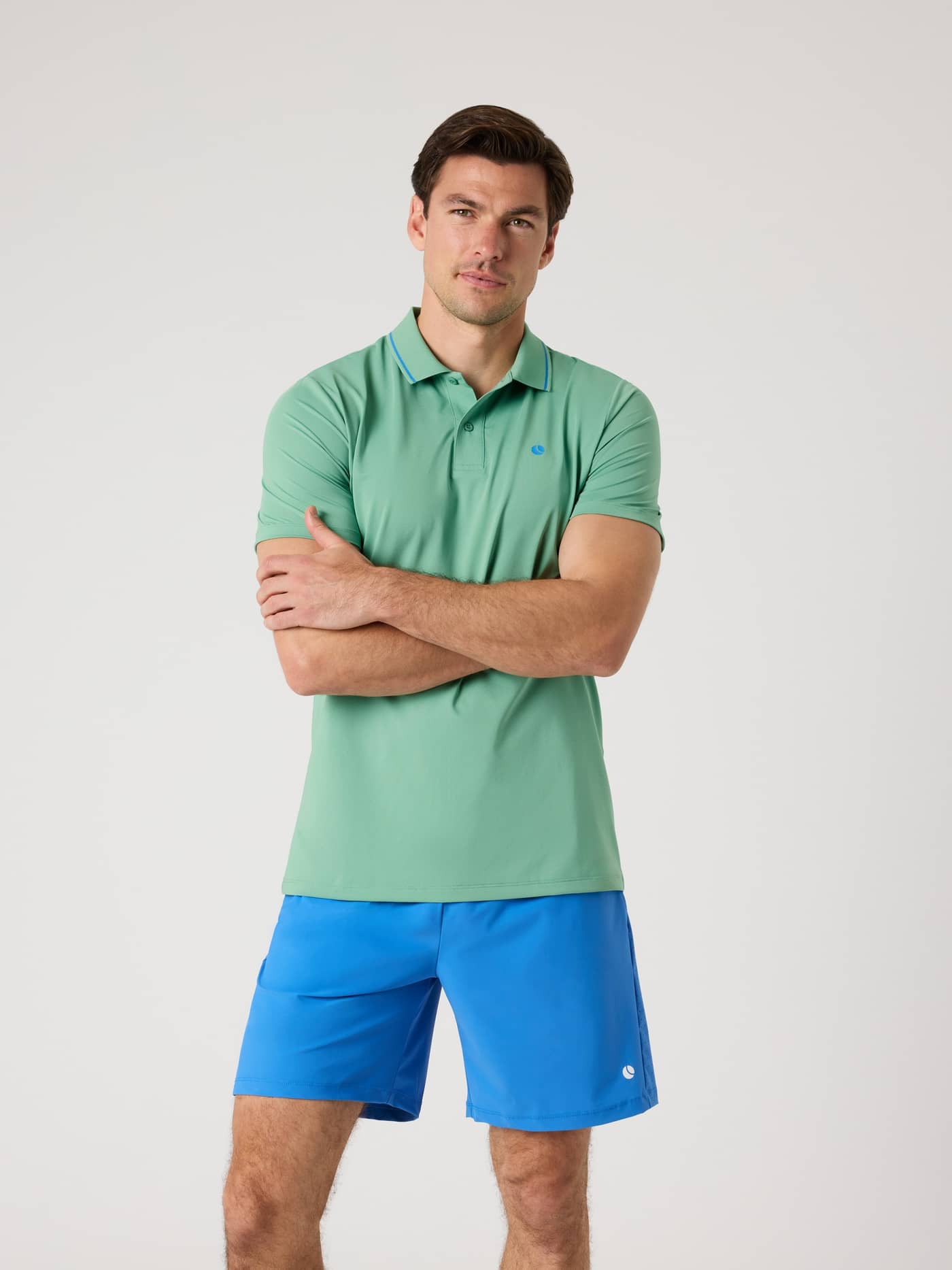 Front view of a man in the Malachite Green (Green) Ace Polo Shirt, a functional recycled polyester tennis top with blue logo. - Image 1