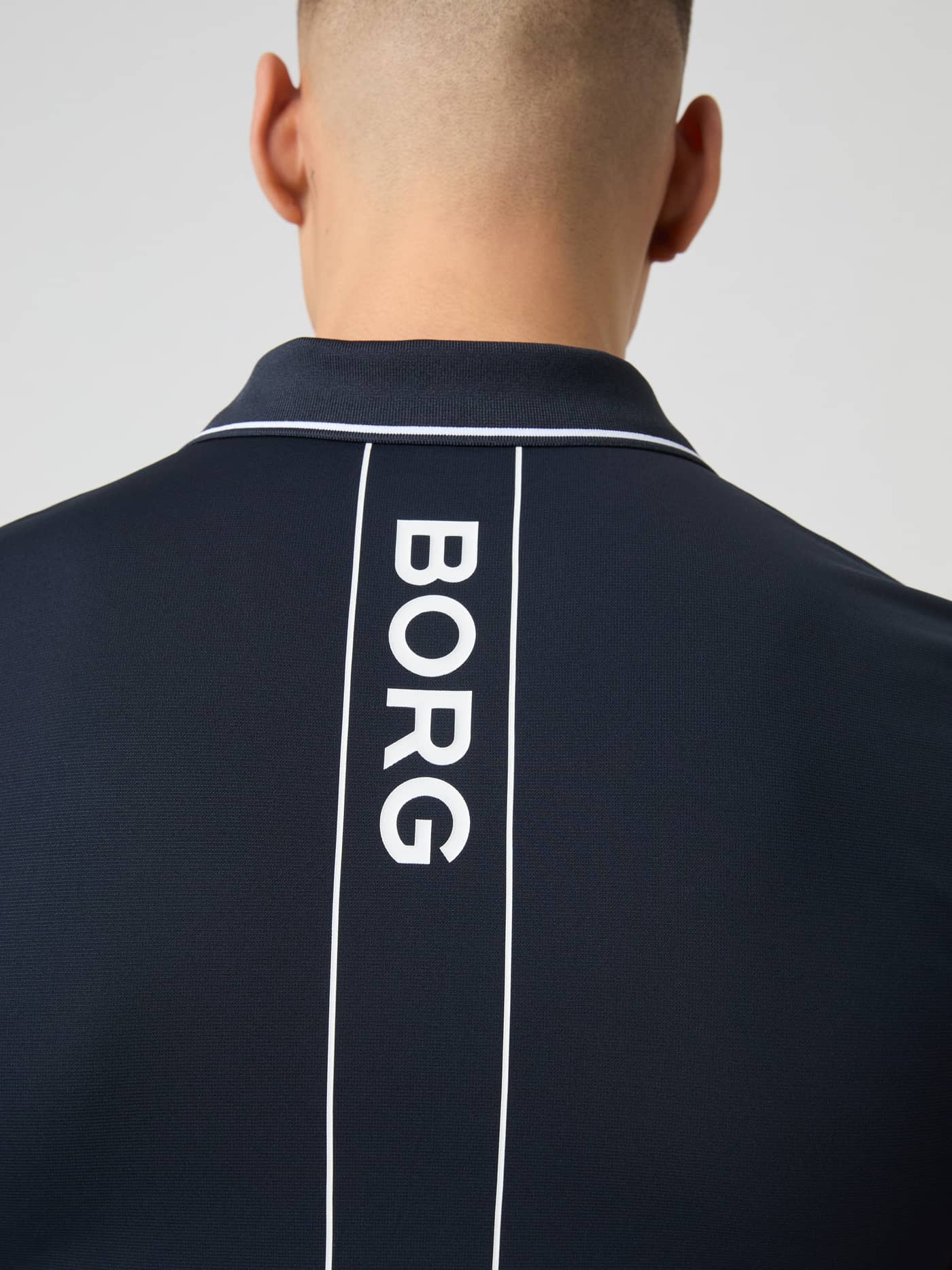Närbild på ryggen av en modell i Ace Polo Shirt i Night sky (Marinblå) med en vertikal BORG-logotyp för tennis. - Image 4