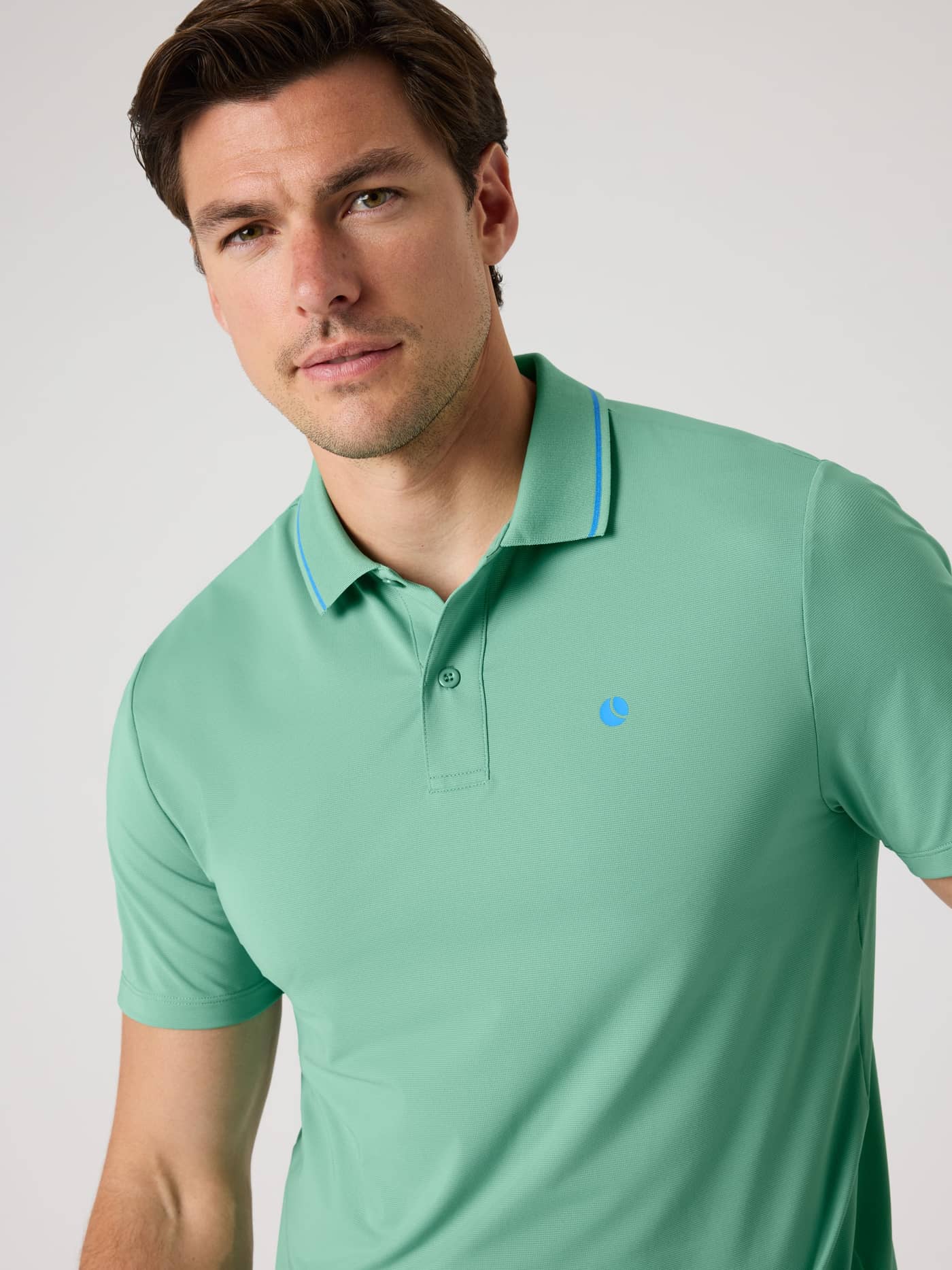 Front view of a man wearing the breathable tennis Ace Polo Shirt in Malachite Green (Green) with a blue tennis ball logo. - Image 5