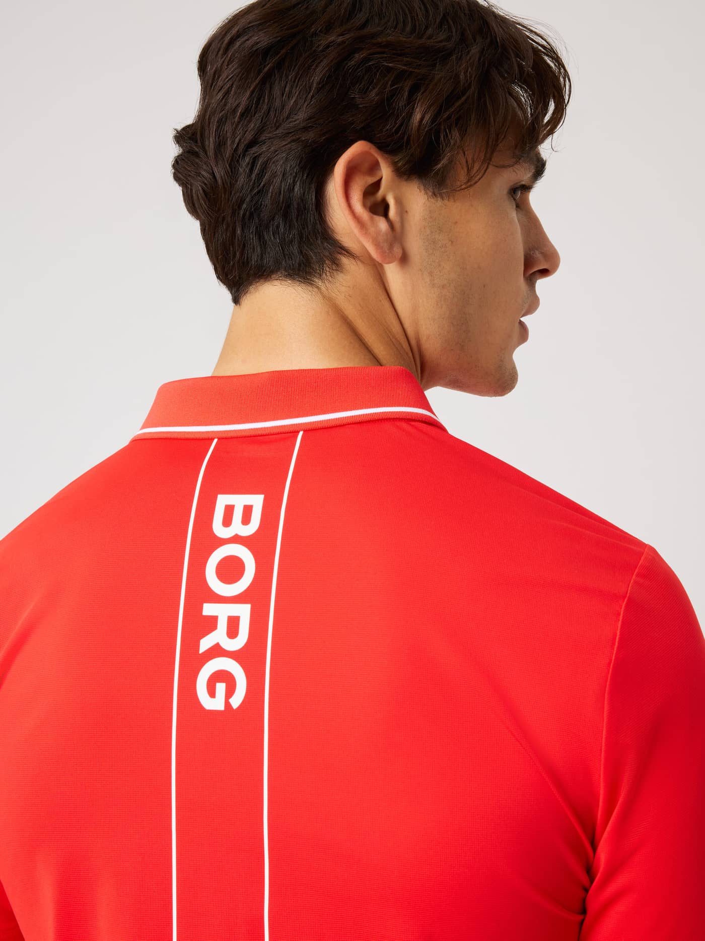 Back view of the Ace Polo Shirt in Flame Scarlet (Red) for tennis, featuring a vertical white Borg logo print. - Image 5