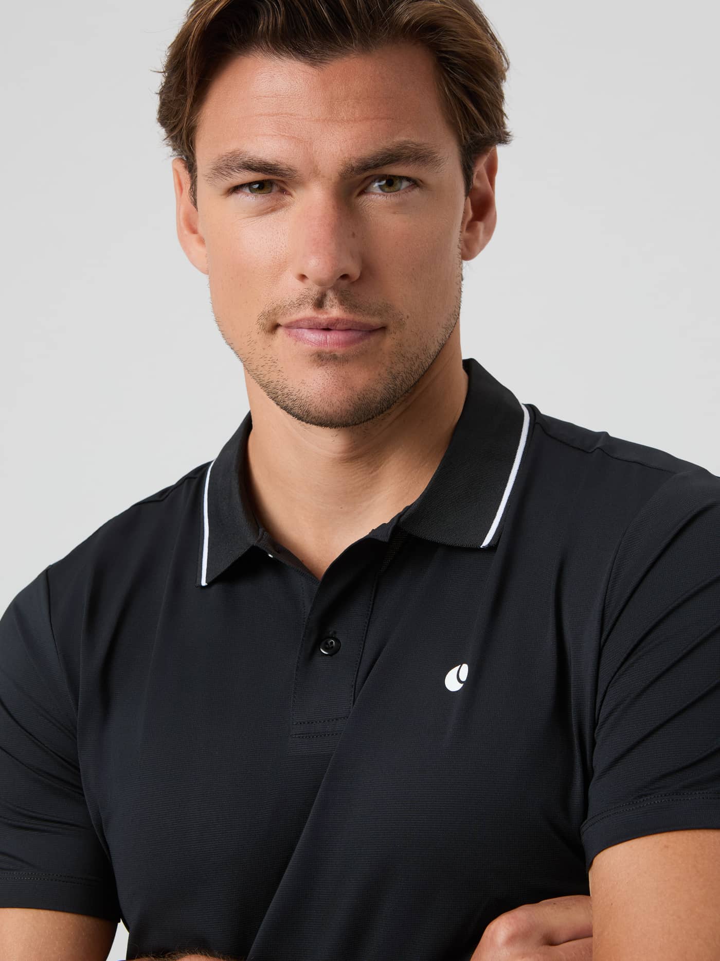 Close-up of a model wearing the black Björn Borg Ace Polo Shirt, showing the collar with white trim and chest logo. - Image 4