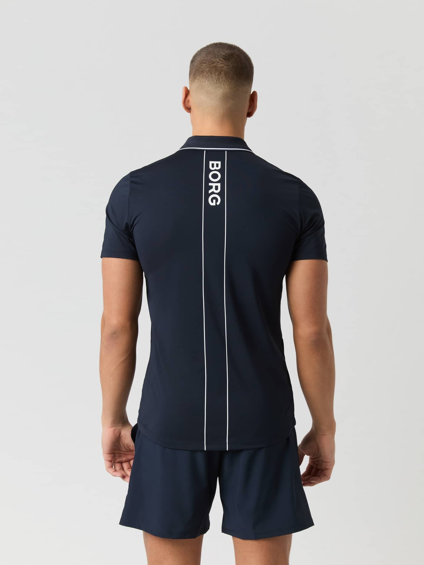 Ace Polo Shirt i Night sky (Marinblå) för tennis sedd bakifrån med en vit vertikal logotyp och rand längs ryggen. - Image 2