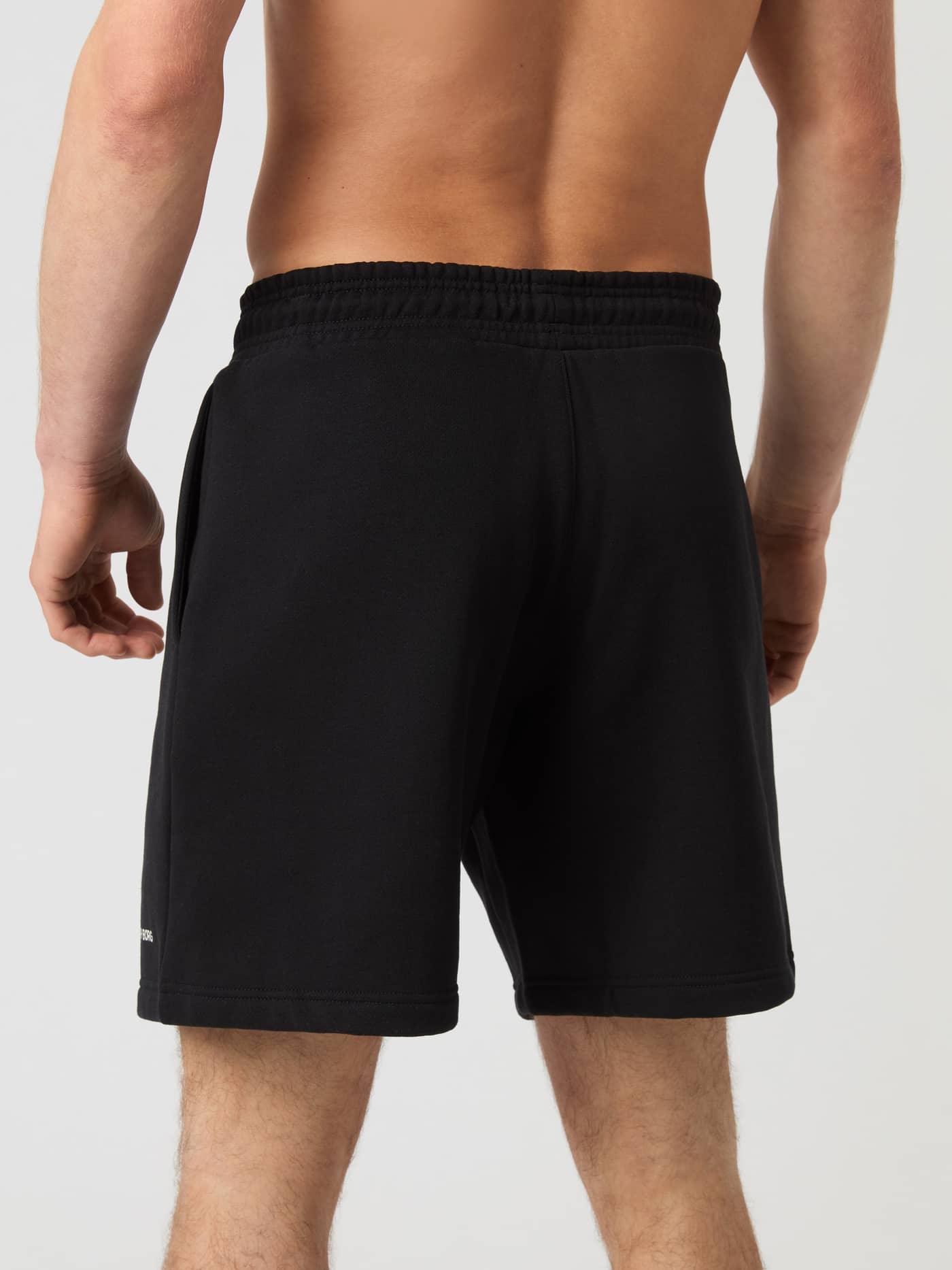 Back view of a man wearing the heavy fleece Björn Borg Oversized Sweatshorts in Black Beauty (Black) with a white logo. - Image 2