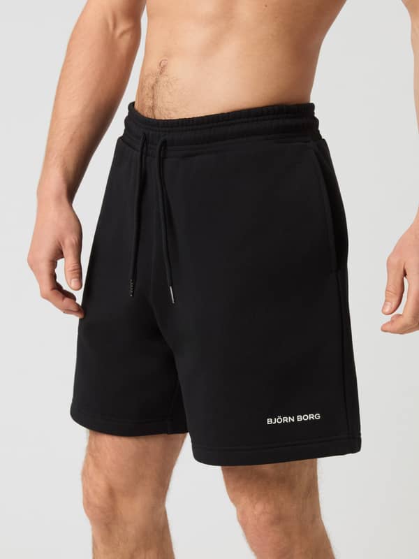 Borg Oversized Sweatshorts i Black Beauty (Svart) i kraftig fleece med vit logotyp på en man sedd framifrån.