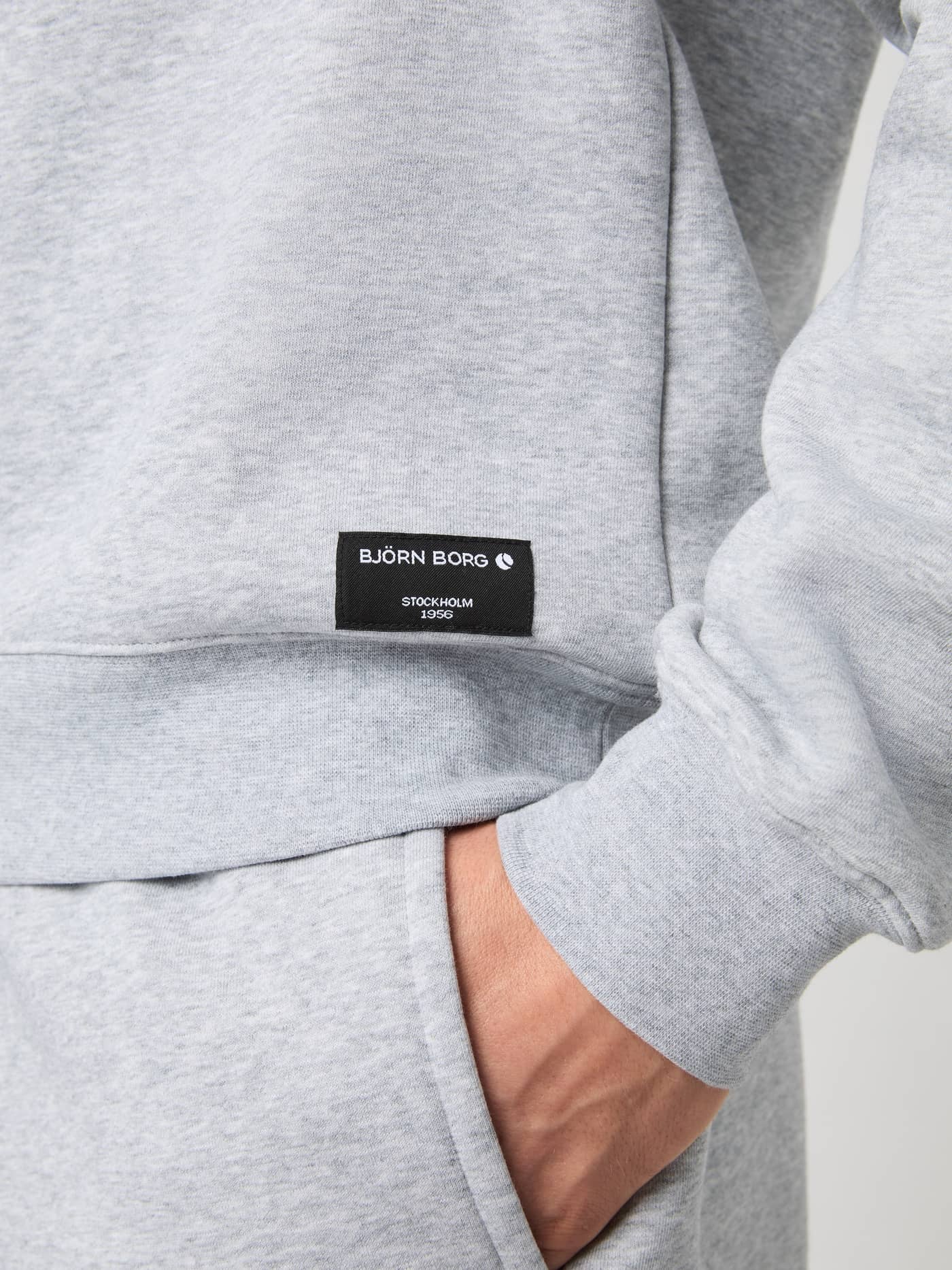 Detail van het Björn Borg Centre Sweatshirt in Light Grey Melange (Grijs) met een zwart geweven logolabel op de heup. - Image 5