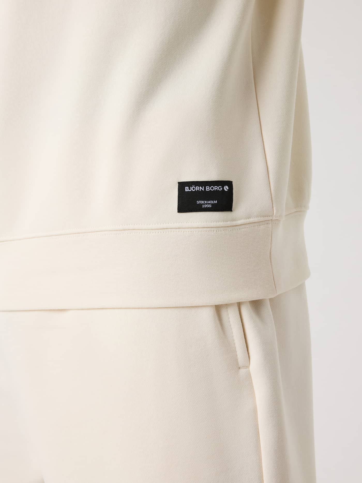 Gedetailleerde close-up van het Björn Borg Centre Sweatshirt in Tofu (Wit) met het zwarte geweven logolabel. - Image 4
