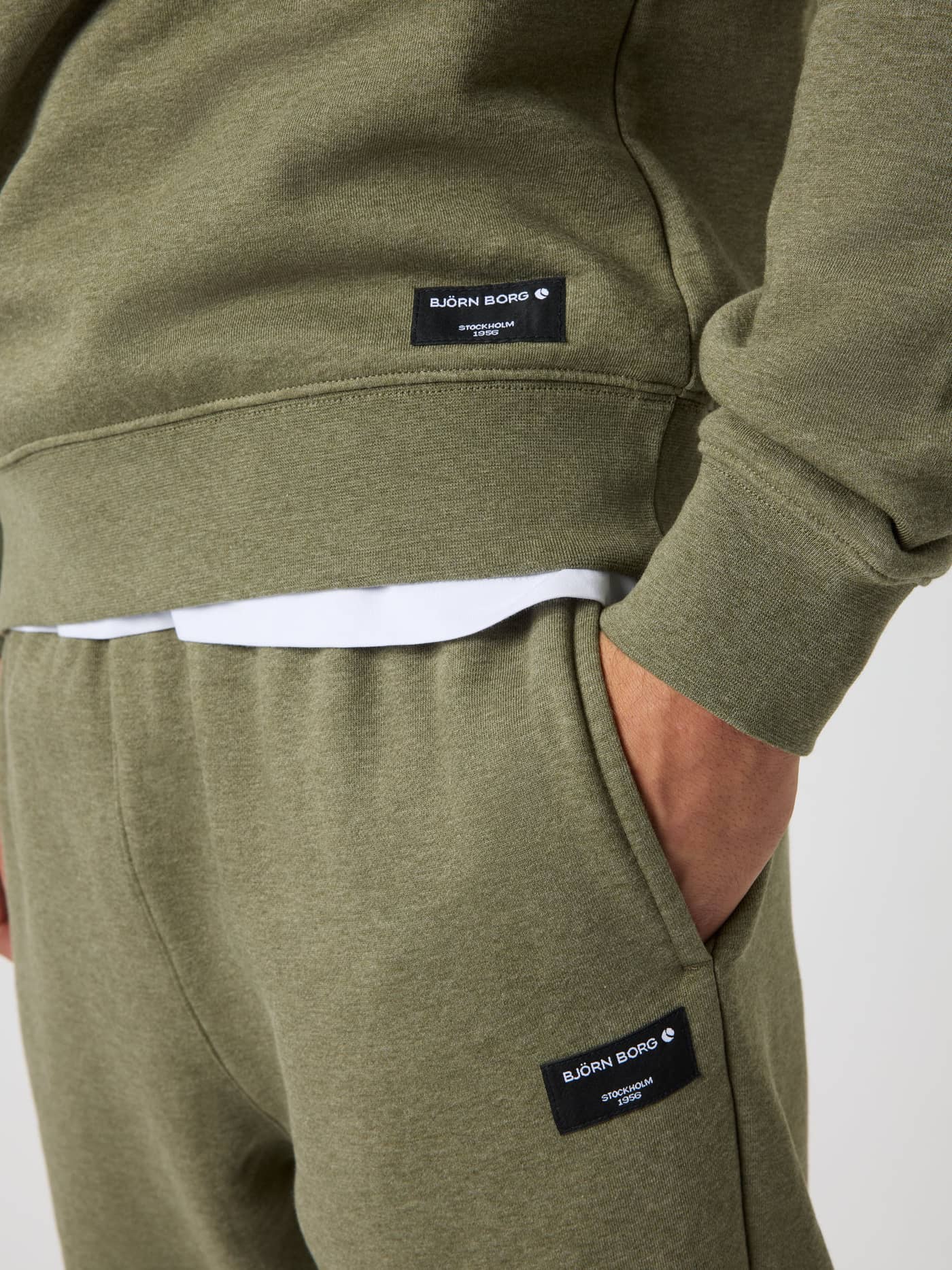 Close-up of the Centre Sweatshirt in Winter Moss Melange (Green) featuring a black woven logo label and ribbed waist. - Image 4