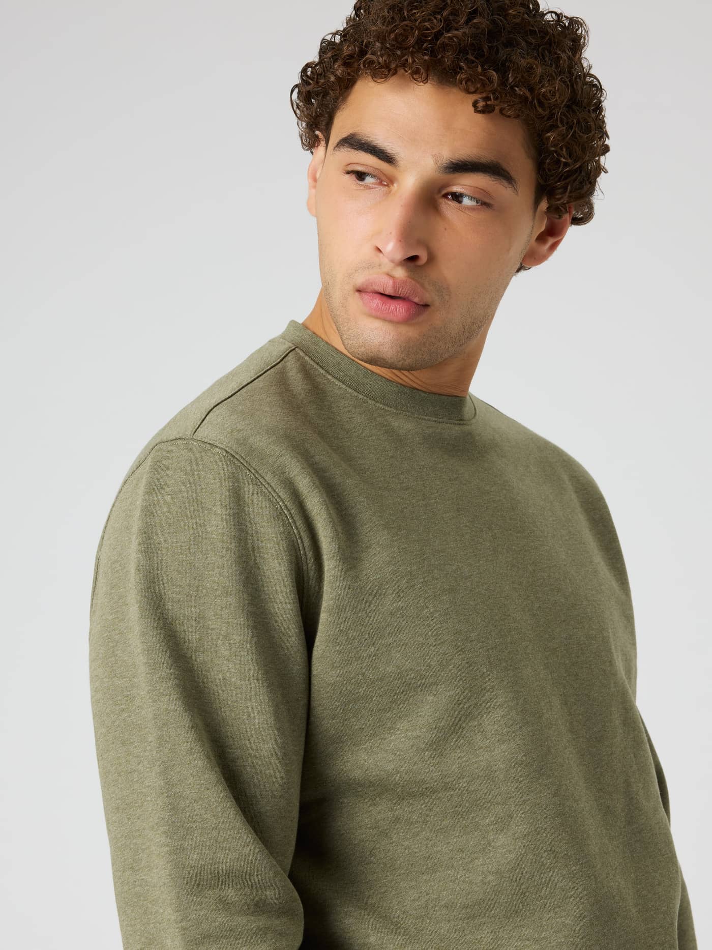 Close-up of a man wearing the Centre Sweatshirt in Winter Moss Melange (Green) with a classic ribbed round neck. - Image 5
