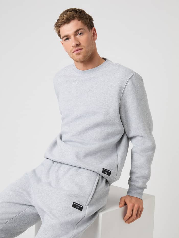 Model sitting down, wearing the Björn Borg Centre Sweatshirt and matching sweatpants in light grey melange.