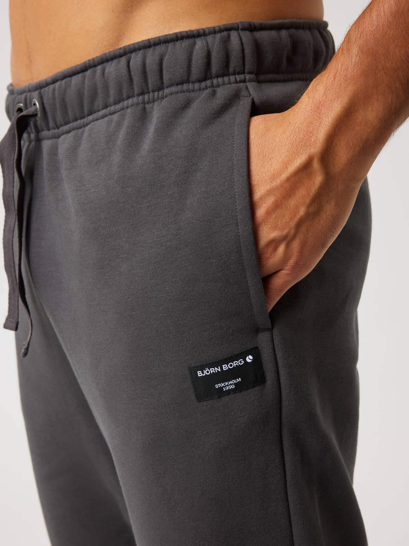 Close-up side view of the Centre Sweatpants in Asphalt (Black) with a side pocket and a black logo label with white text. - Image 4