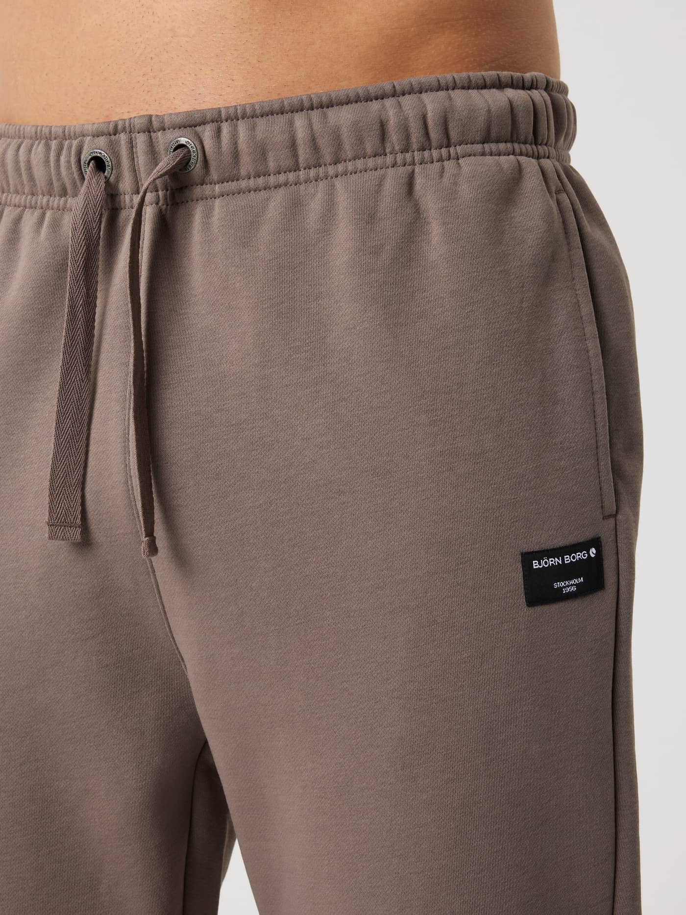 Close-up of the cotton-blend Centre Sweatpants in Falcon (Brown) for men, featuring a black logo label and drawstring. - Image 4