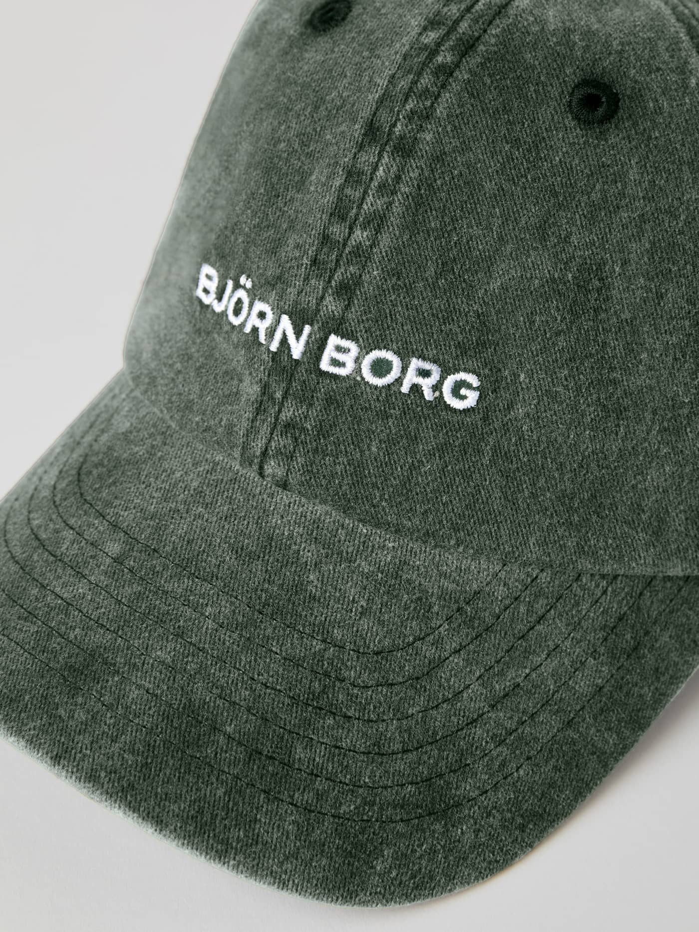 Nærbilde av Borg Washed Cap i Balsam Green (Grønn) i økologisk bomull med vasket effekt og hvit brodert logo. - Image 3