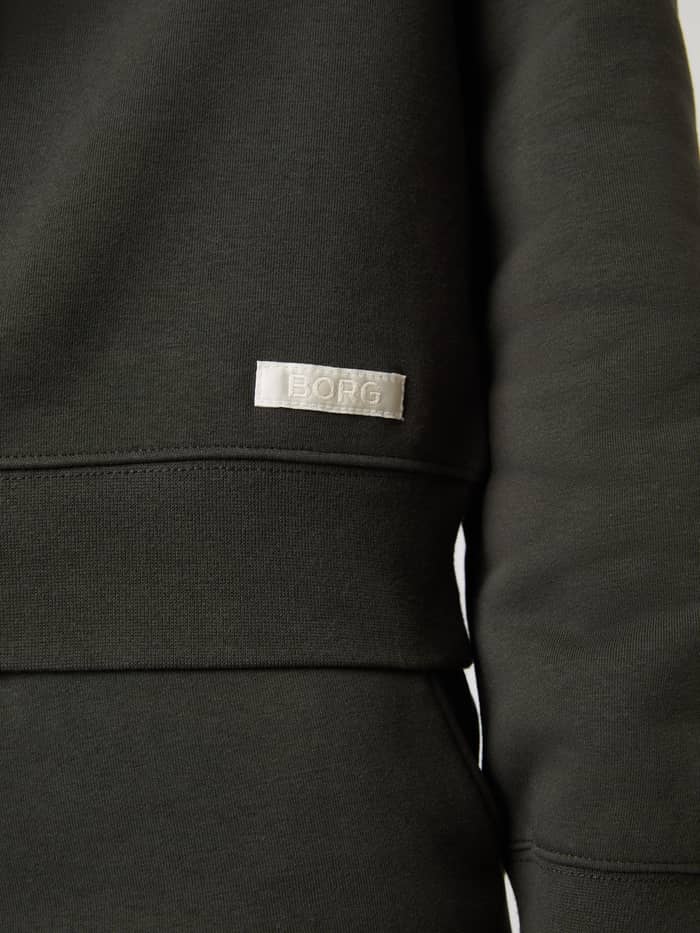 Nahaufnahme des weichen Centre Sweatshirt für Damen in Peat (Grün) mit weißem Logo-Webetikett und geripptem Saum. - Image 5