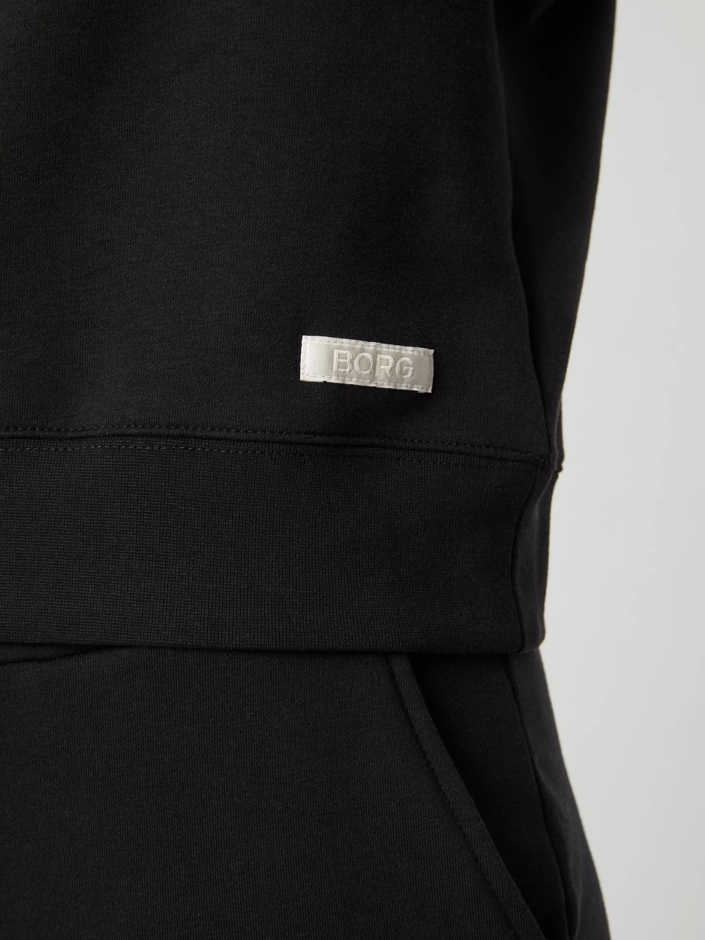 Detailed shot of the white woven logo on the hip of the women's Björn Borg Centre Sweatshirt in Black Beauty (Black). - Image 5