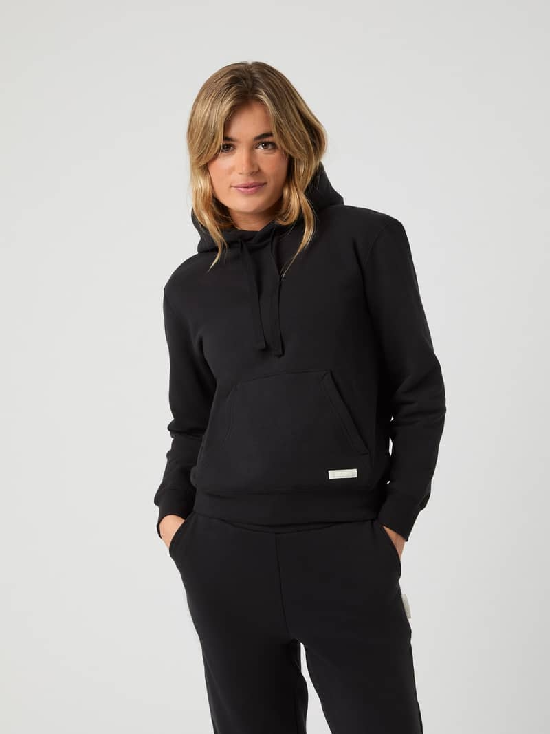 Front view of a woman wearing the oversized Björn Borg Centre Hoodie in Black Beauty (Black) with a kangaroo pocket.