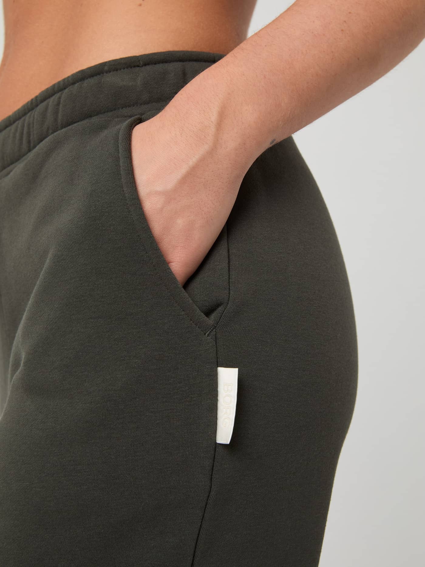 Close-up of the Björn Borg Centre Sweatpants in Peat (Green), highlighting the stylish fit, pocket, and white logo label. - Image 4
