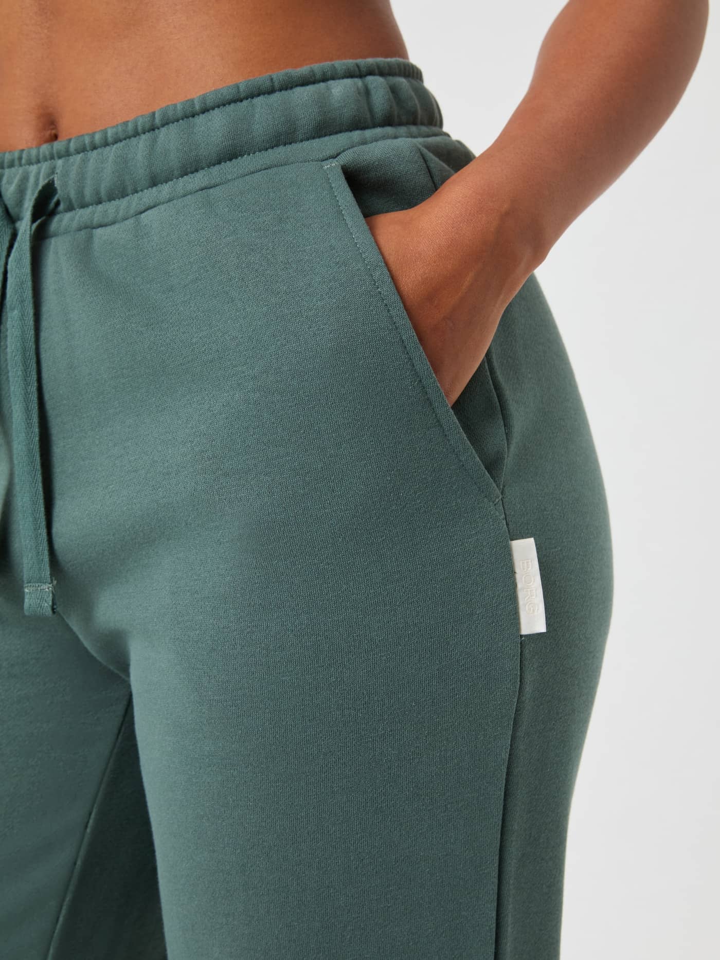 Detailed close-up of the women's Björn Borg Centre Sweatpants in Balsam Green (Green) showcasing the pocket and white logo. - Image 4