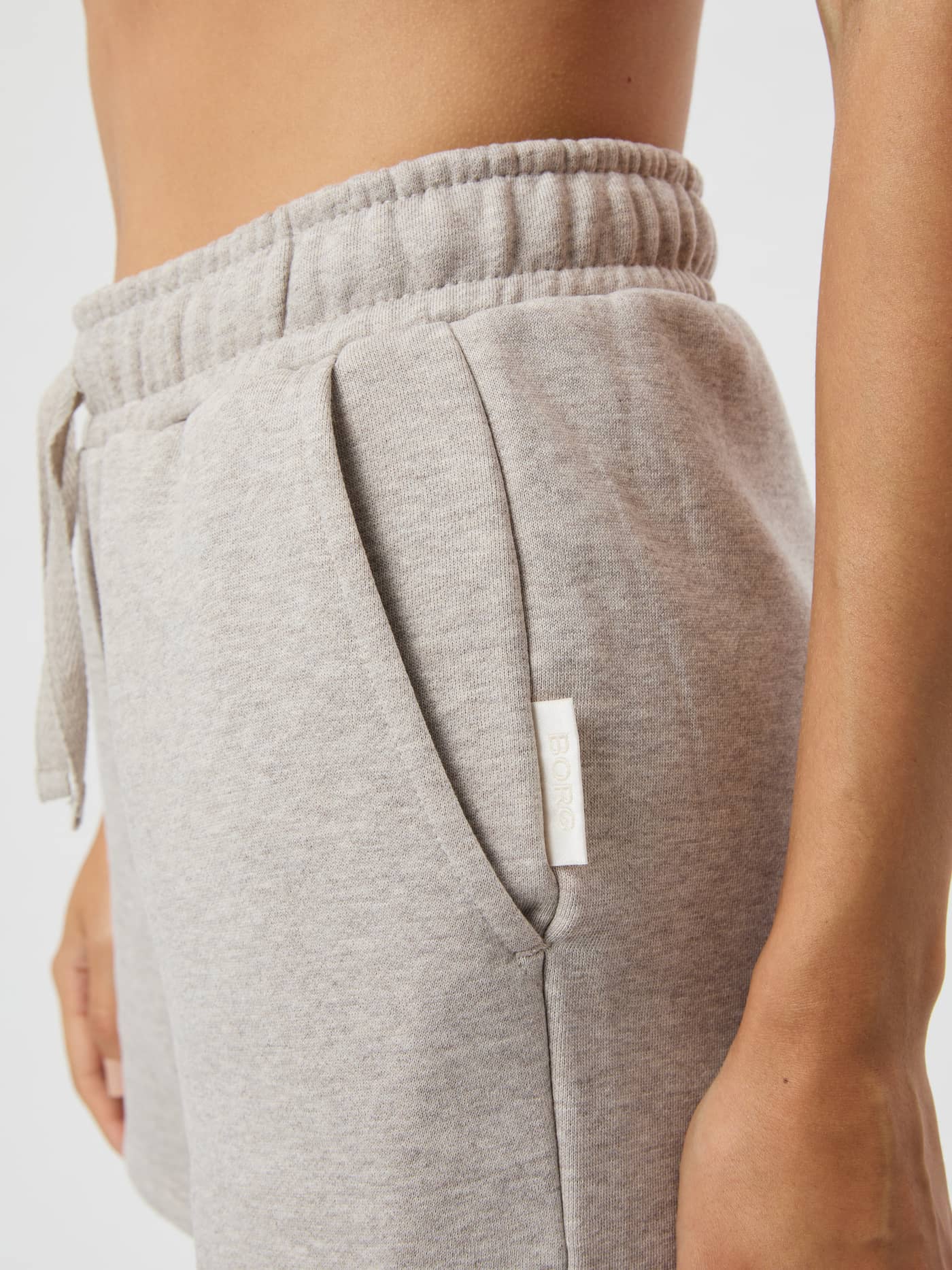 Sidovy av Centre Sweatshorts i Light Brown Melange (Beige) med sidoficka och vit logoetikett. - Image 4