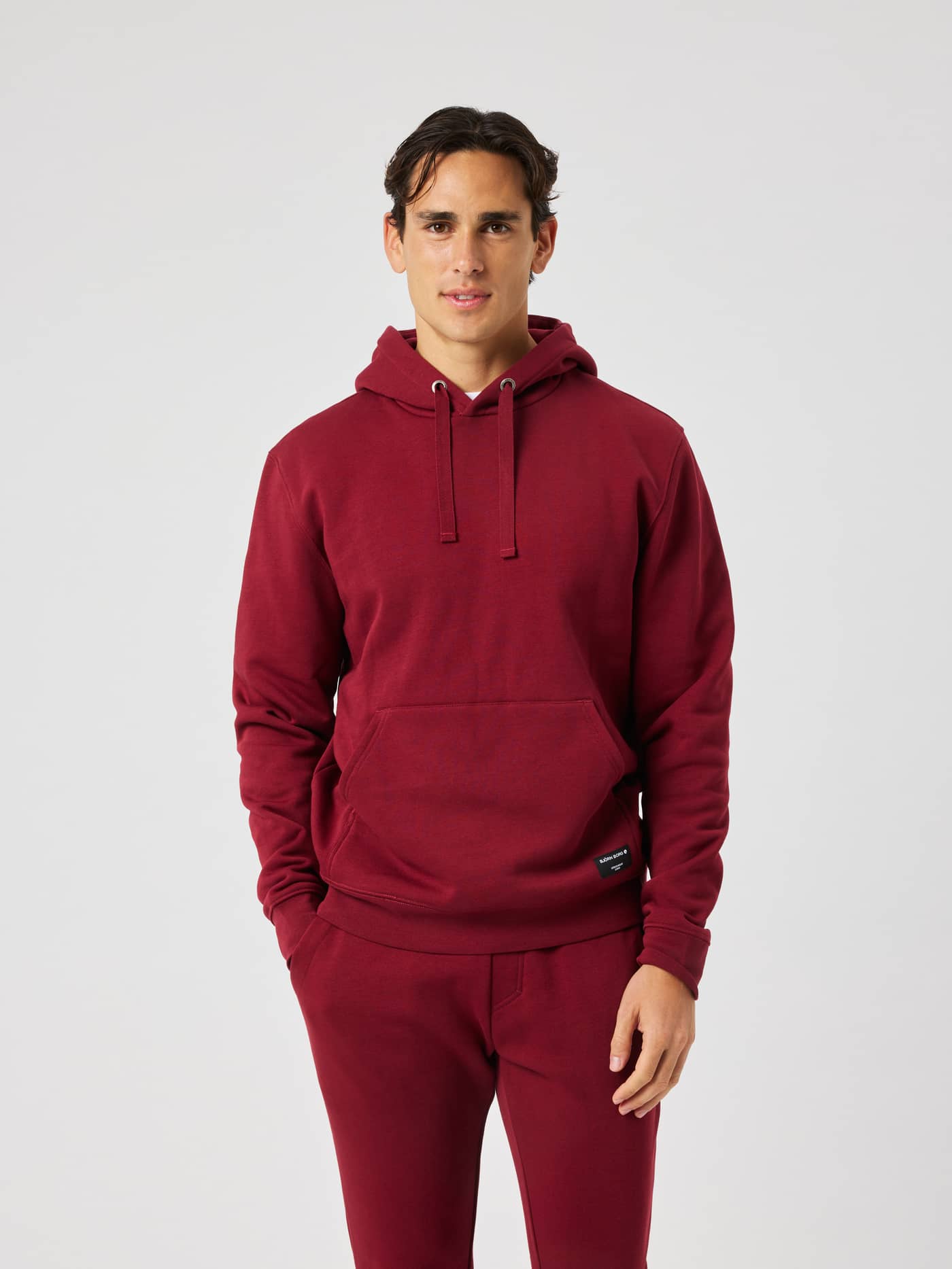 Man wearing the Centre Hoodie in Cabernet (Red) featuring a double layer hood and a front kangaroo pocket for leisure. - Image 2