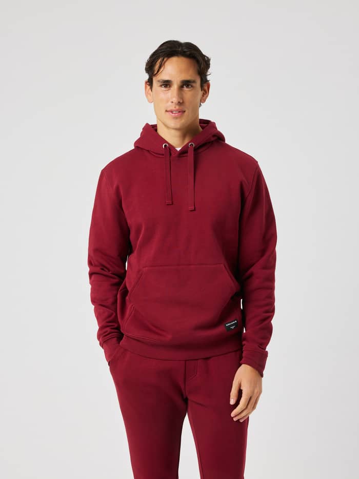 Man wearing the Centre Hoodie in Cabernet (Red) featuring a double layer hood and a front kangaroo pocket for leisure.