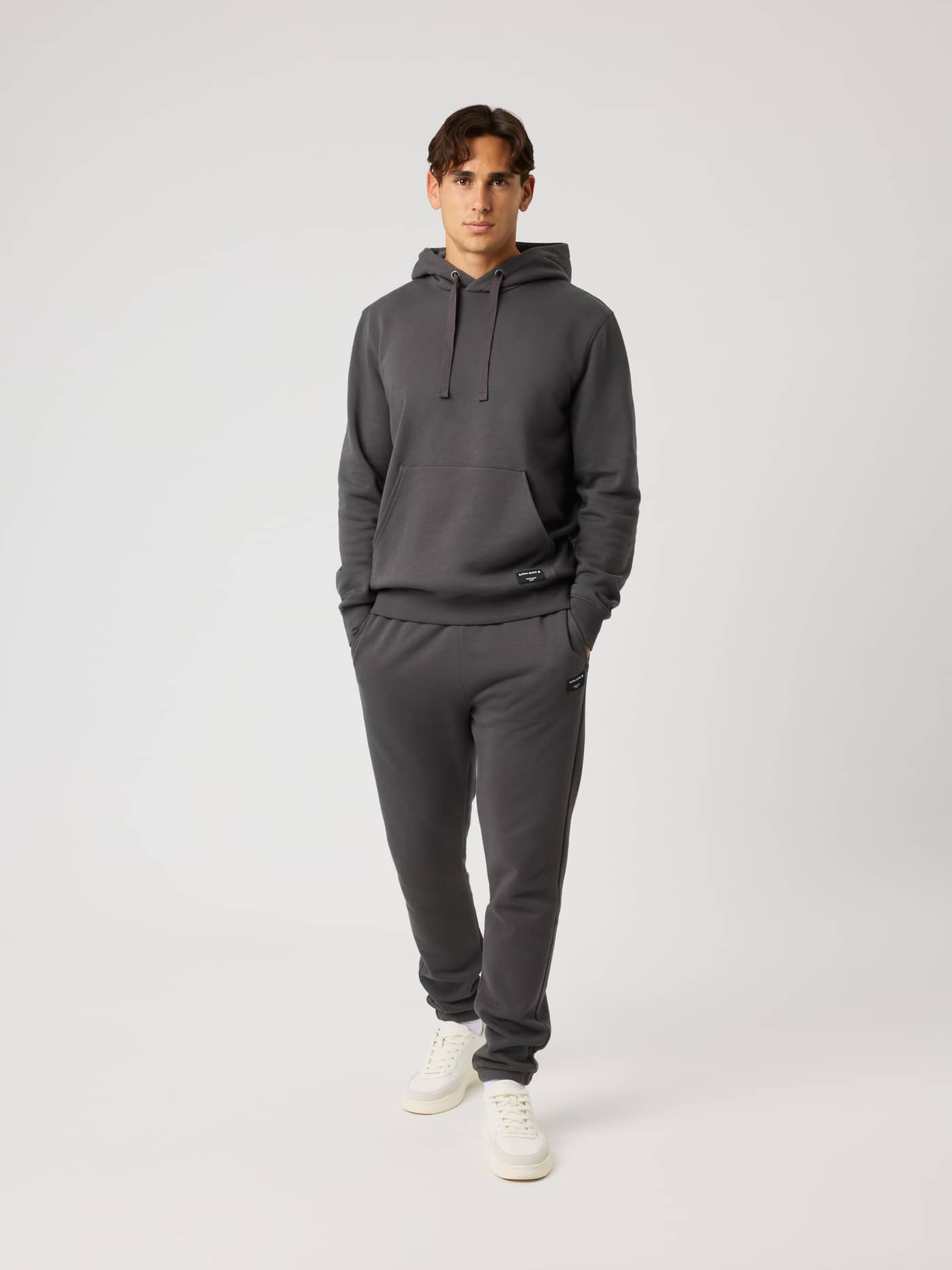 Full-body front view of a model wearing the Centre Hoodie in Asphalt (Grey) with a kangaroo pocket and black logo label. - Image 3