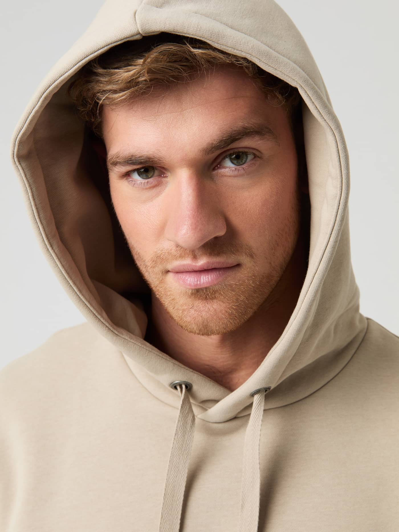 Close-up of a man wearing the beige Björn Borg Centre Hoodie with the hood up, looking at the camera. - Image 4
