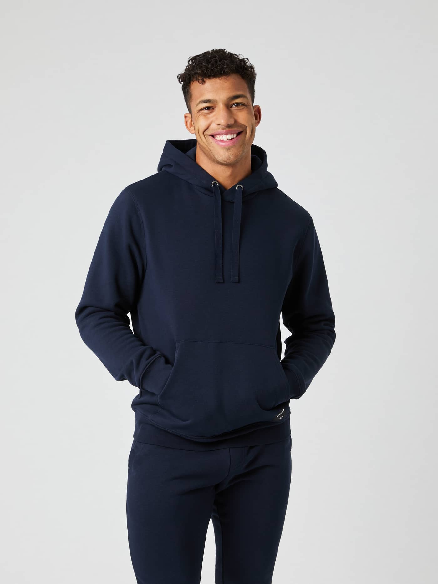 Front view of a smiling male model wearing the navy blue Björn Borg Centre Hoodie with his hands in the pocket. - Image 1