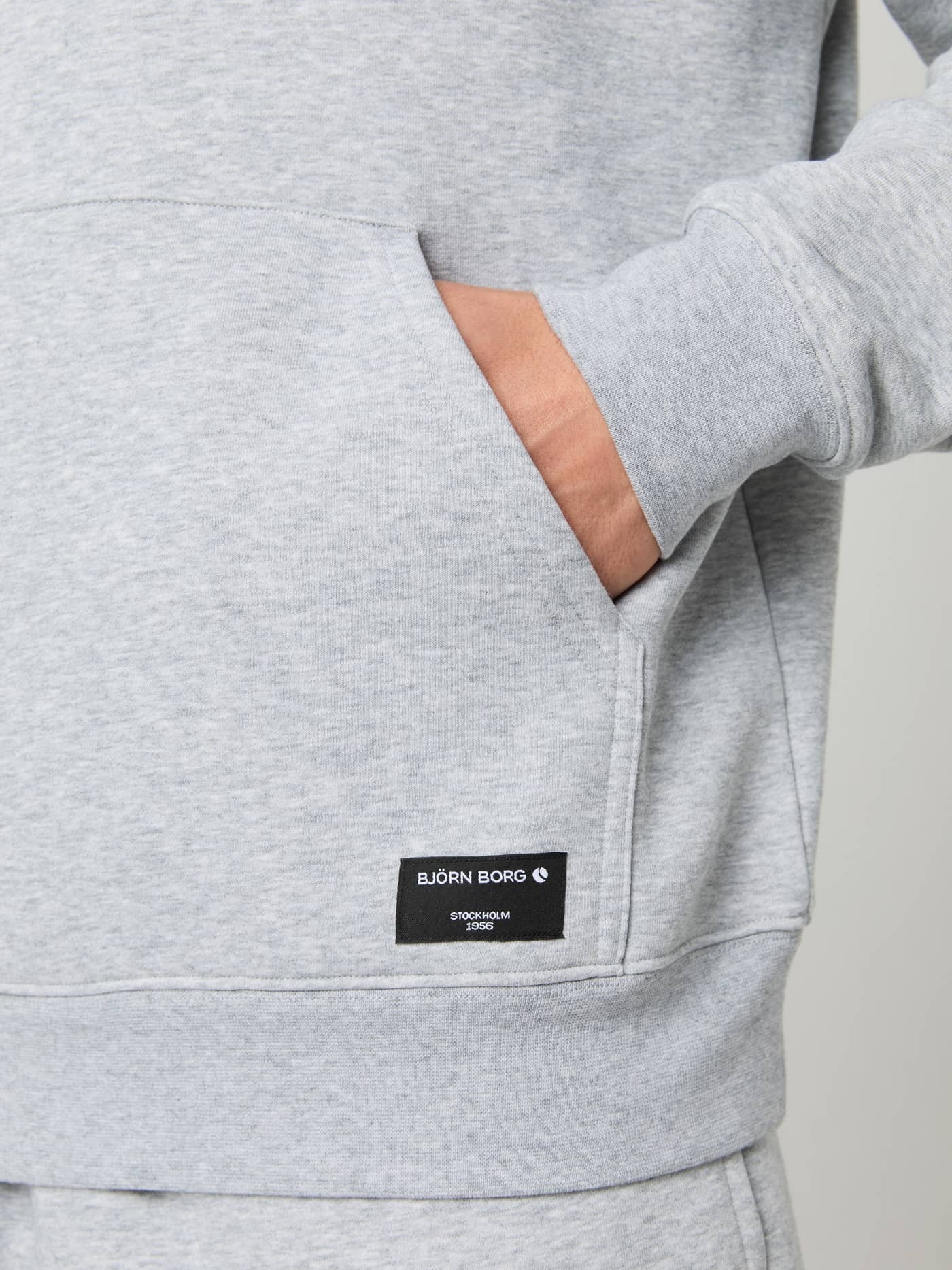Nahaufnahme des Centre Hoodie in Light Grey Melange (Grau) mit Kängurutasche, schwarzem Logo-Patch und stilvollem Fit. - Image 4
