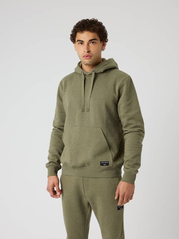 Front view of a model wearing the Centre Hoodie in Winter Moss Melange (Green) with a kangaroo pocket and black logo label.